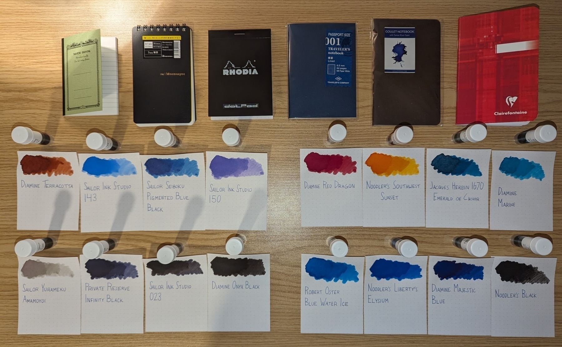 Six pocket notebooks and sixteen different colorful ink swatches arranged on a light wooden desk
