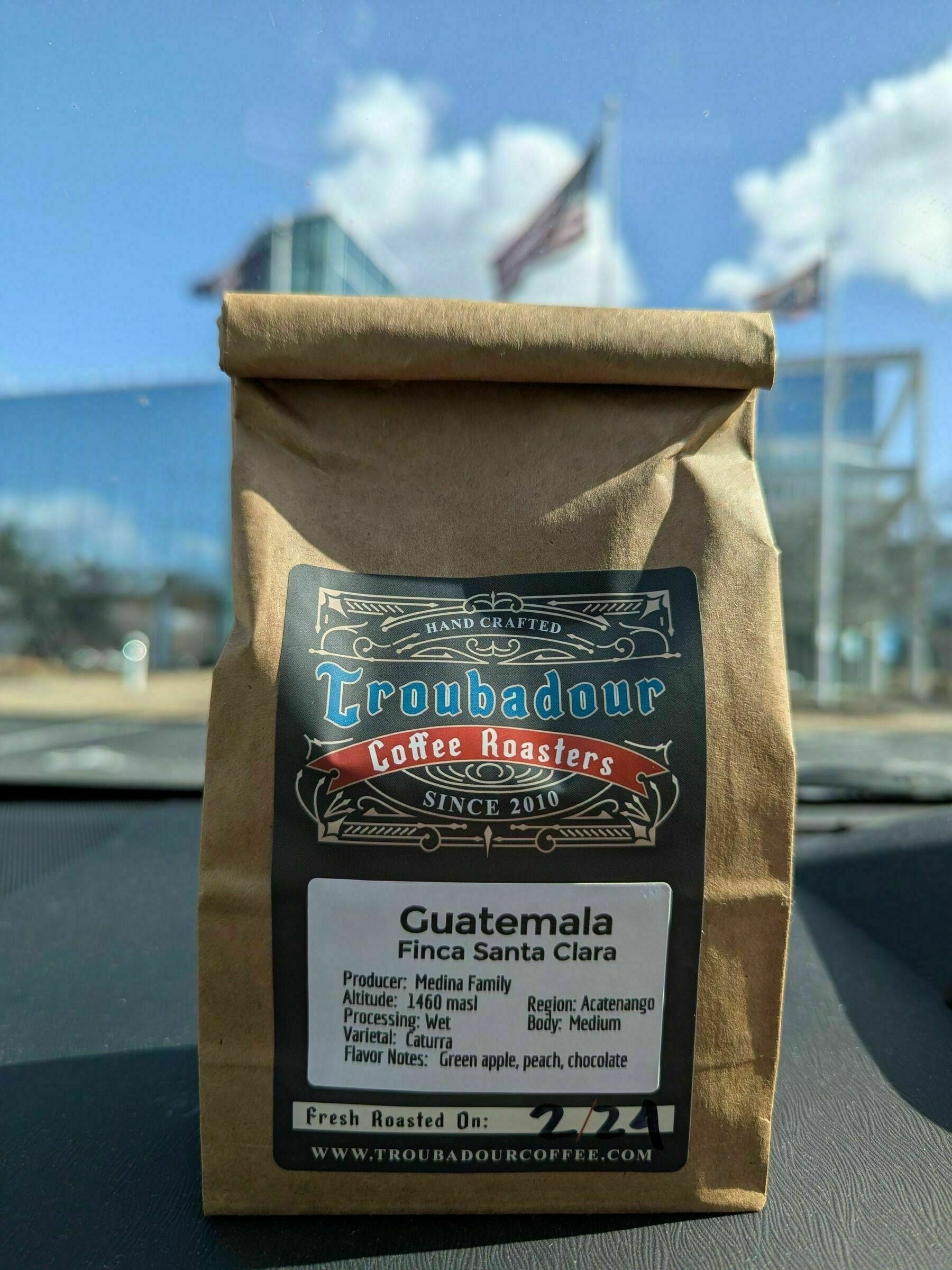 A picture of a bag of coffee sitting on a car dashboard with a bright, blurry background