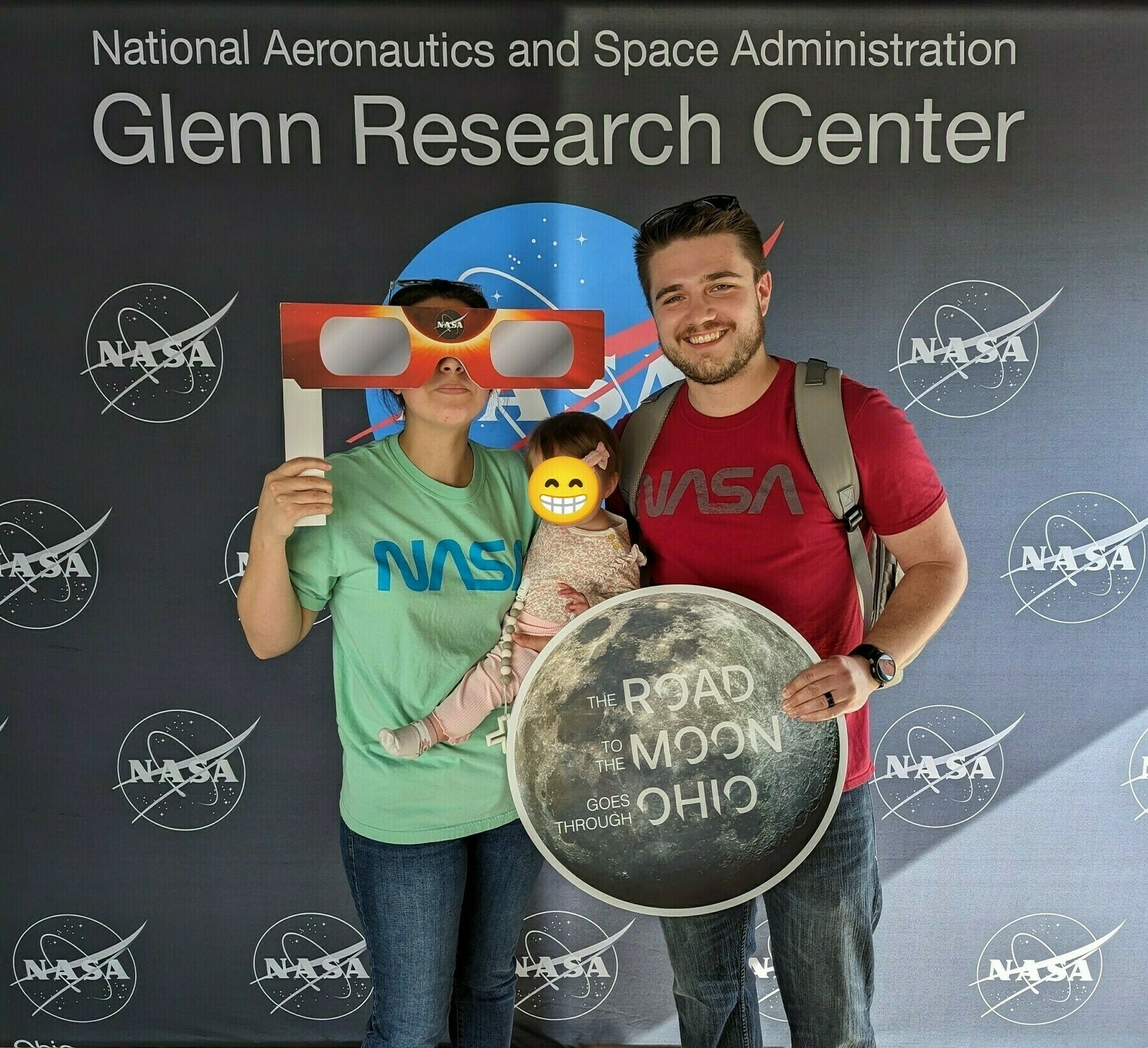 The Weidokal family wearing NASA shirts and posing in front of a NASA Glenn Research Center picture wall wioth NASA logos all over it.