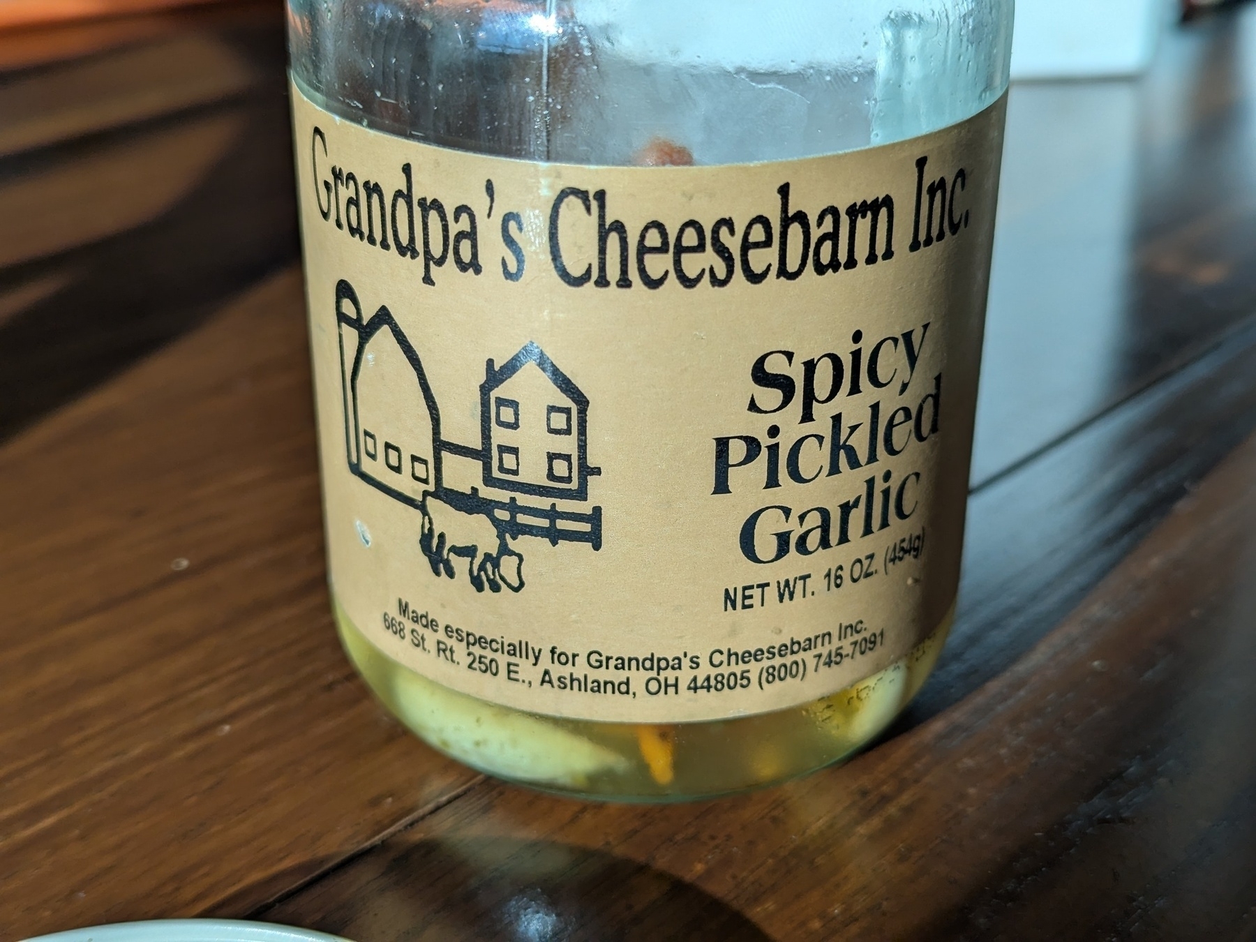 A jar labeled Grandpa's Cheesebarn Inc. Spicy Pickled Garlic is sitting on a wooden surface.