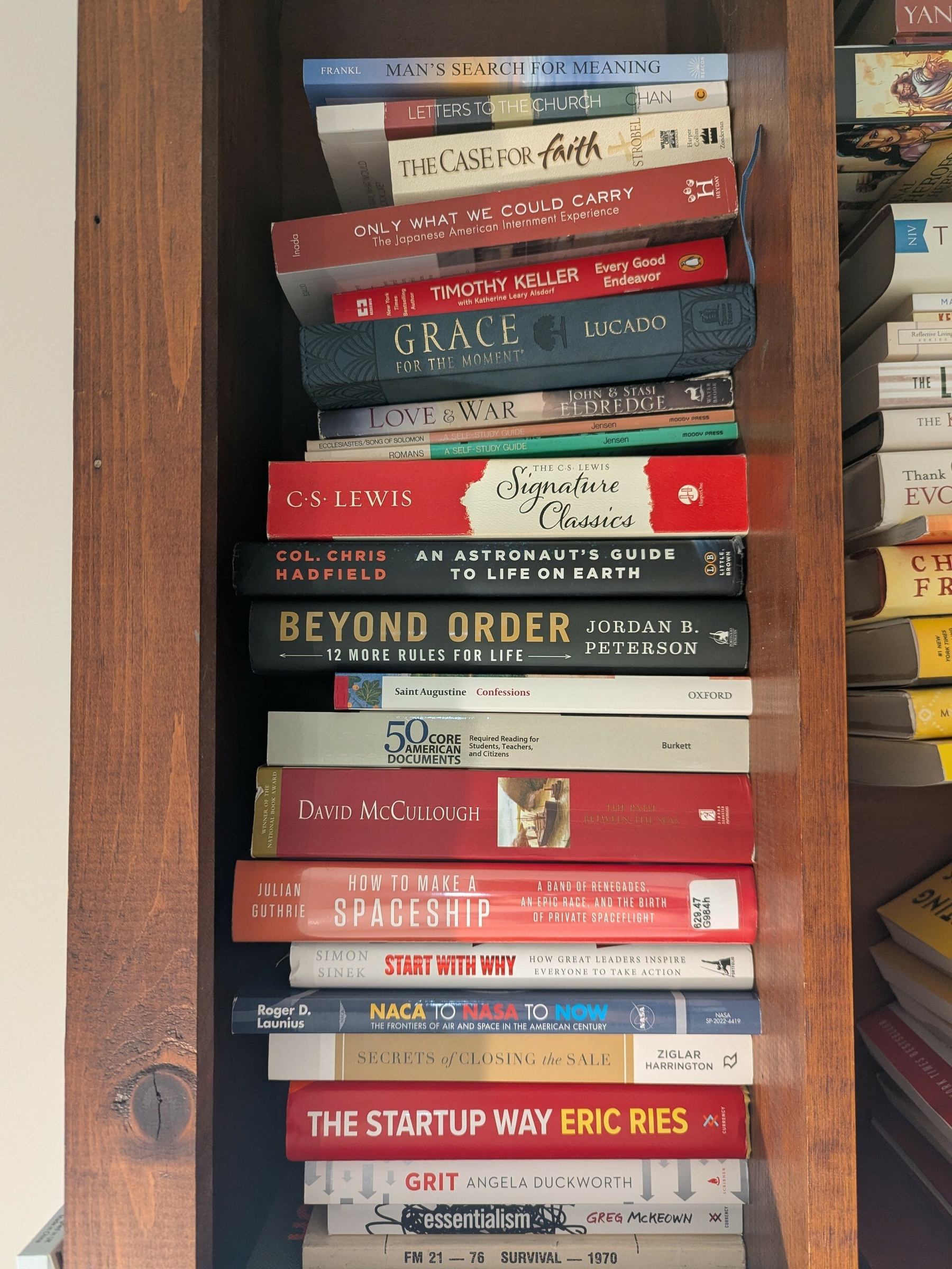 A stack of various books is neatly arranged on a wooden shelf.