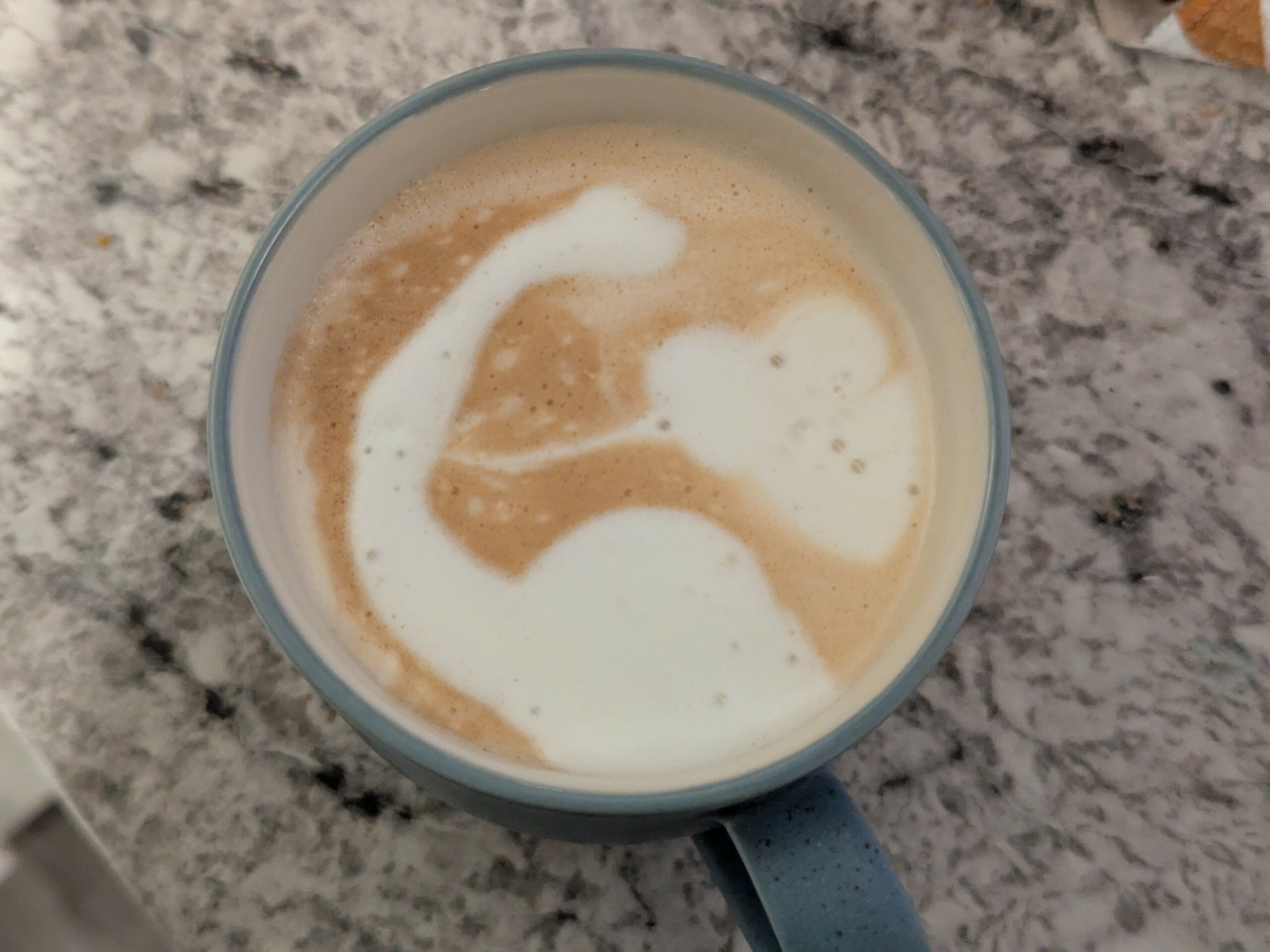 A cup of coffee with latte art resembling a brontosaurus and a heart.