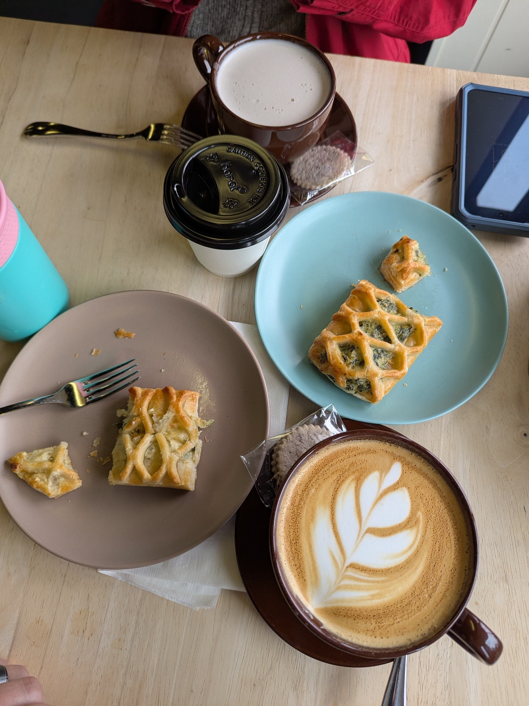 Pastries and drinks, including a latte with latte art, are arranged on a table with plates and cups.