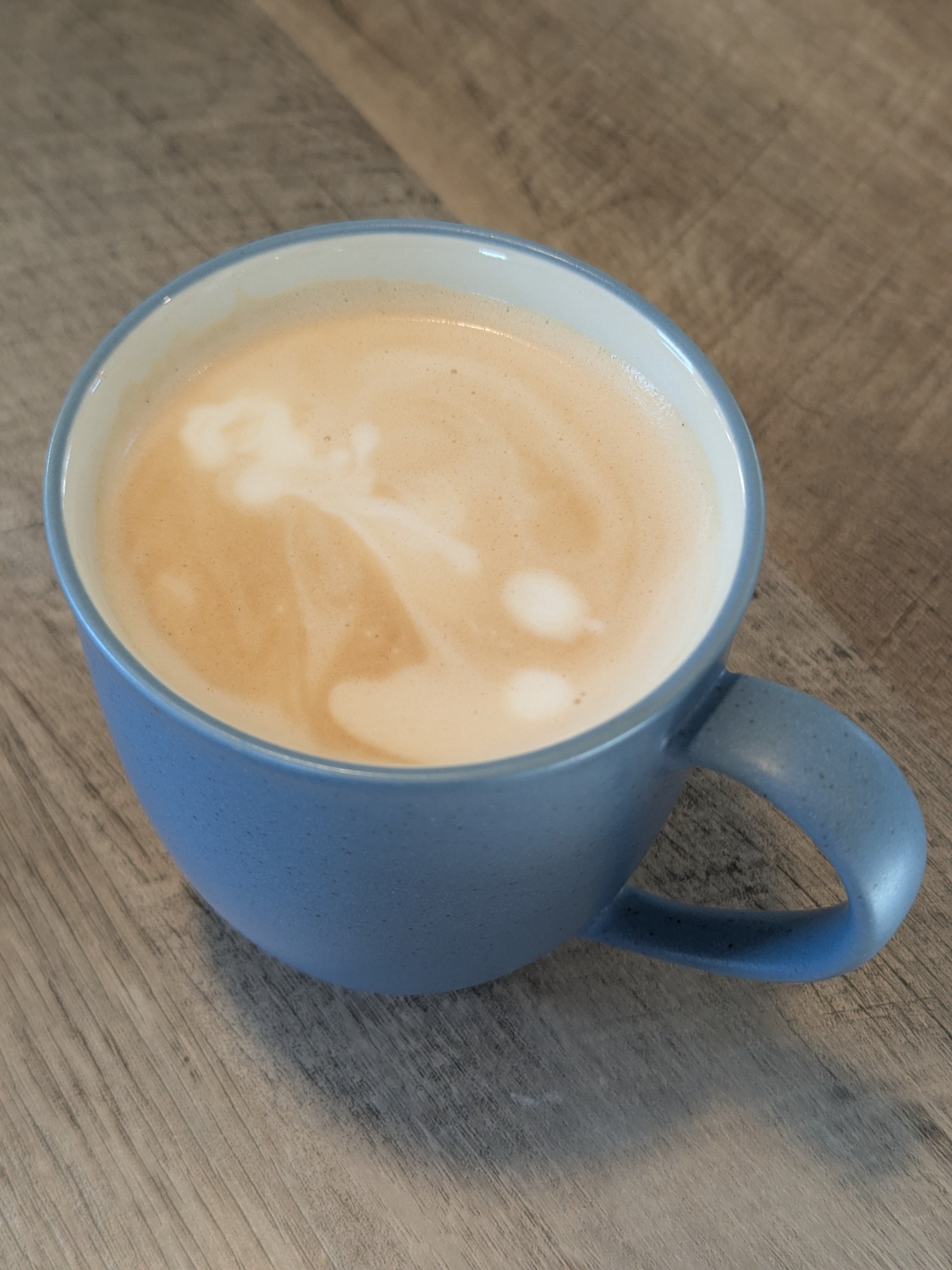 A blue mug filled with frothy coffee sits on a wooden surface.