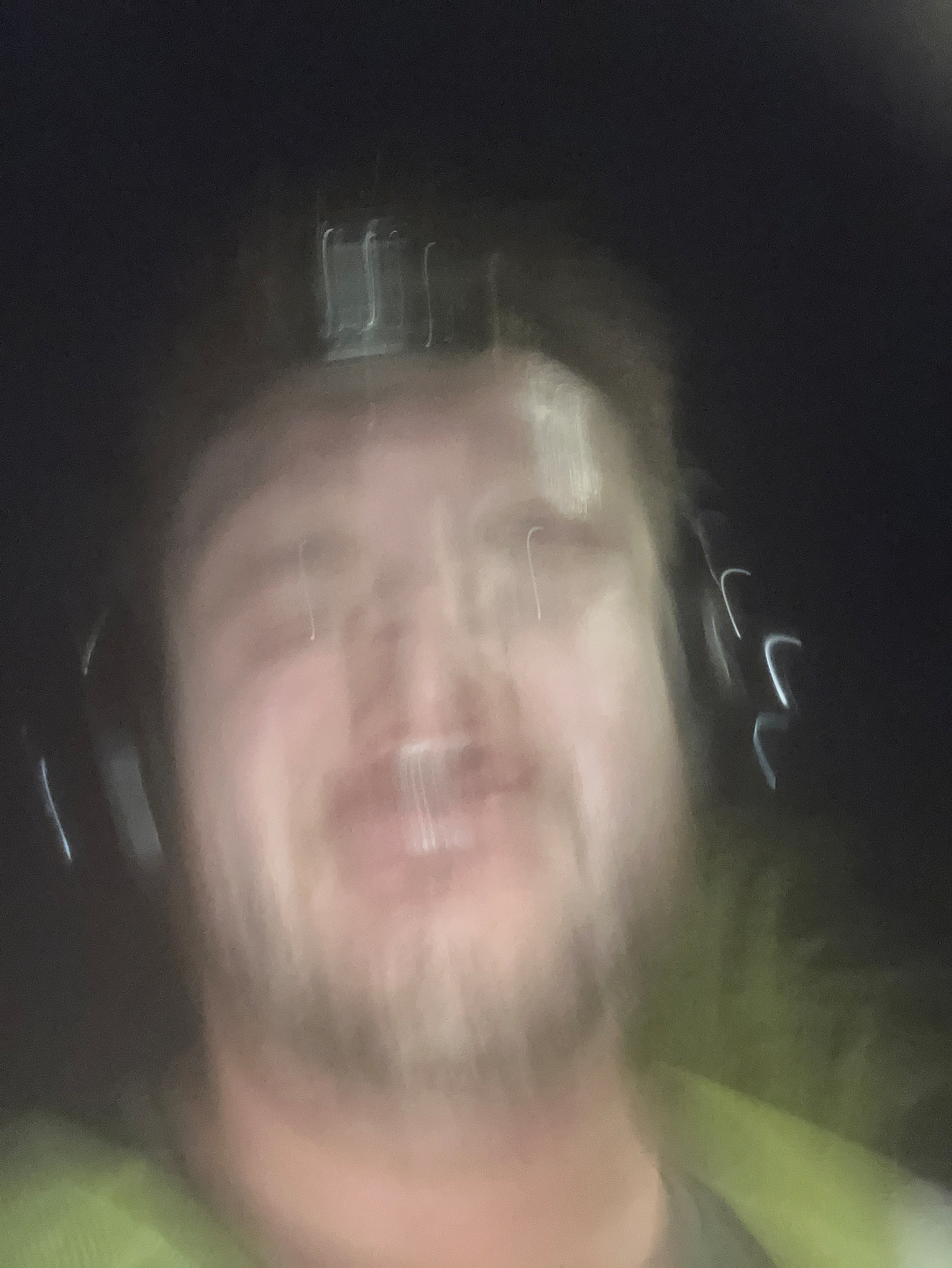 A blurry close-up of a person wearing headphones and a green jacket against a dark background.