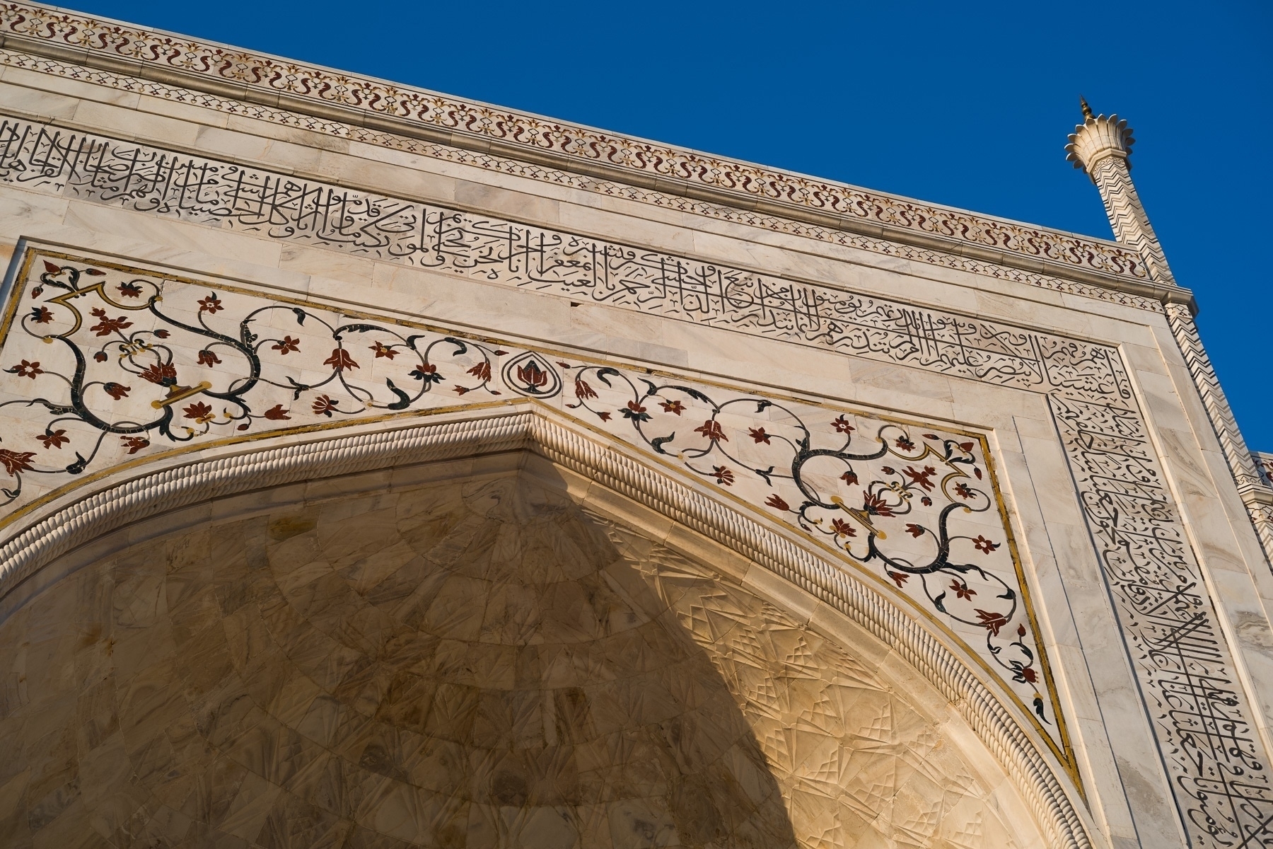Main arch on the front of the Taj Mahal showing the stone inlaid patterns of flowers and inscriptions embedded in the marble.