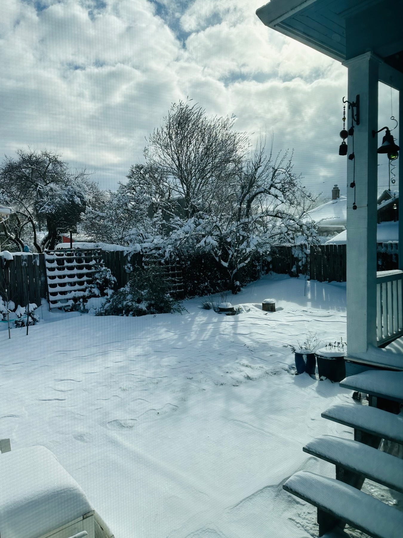 A backyard with snow everywhere. Partly cloudy sky.