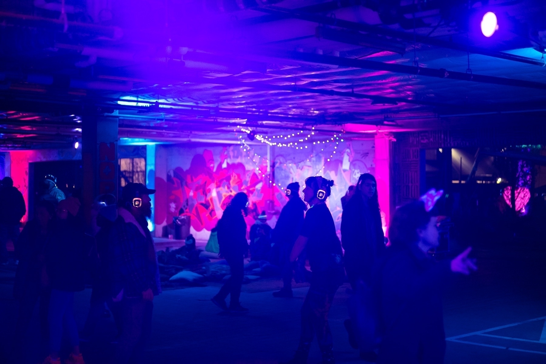 People dancing at a silent disco in a dimly lit space with bright pops of colorful lights.