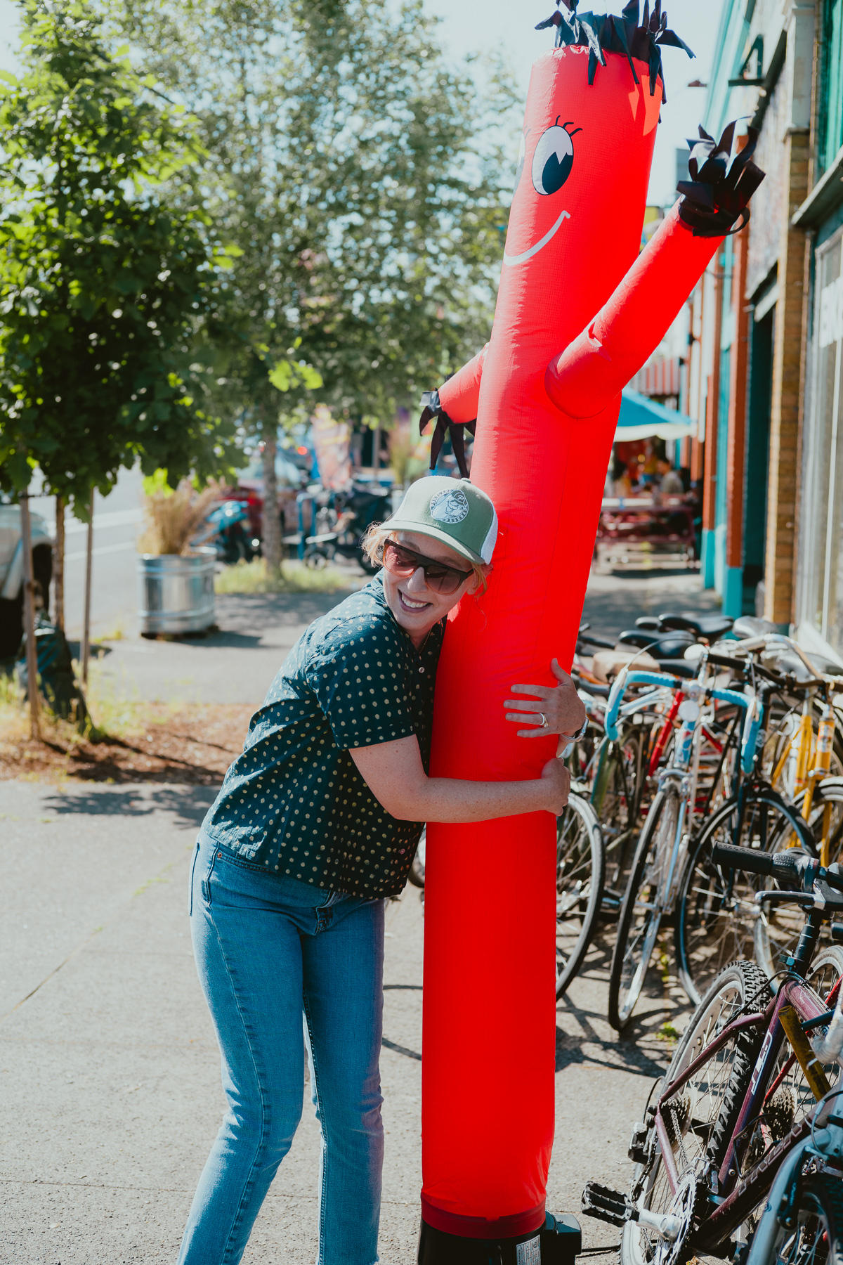 A laughing woman hugs an inflatable tube man on a sidewalk.