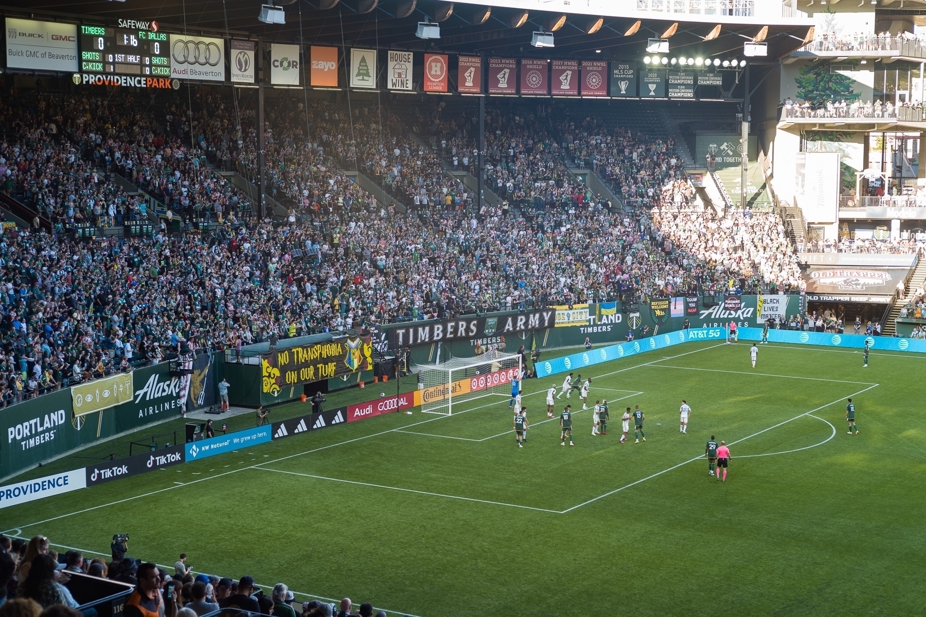 View of a stadium full of people with a banner behind the soccer goal with words that read, “No transphobia on our turf”
