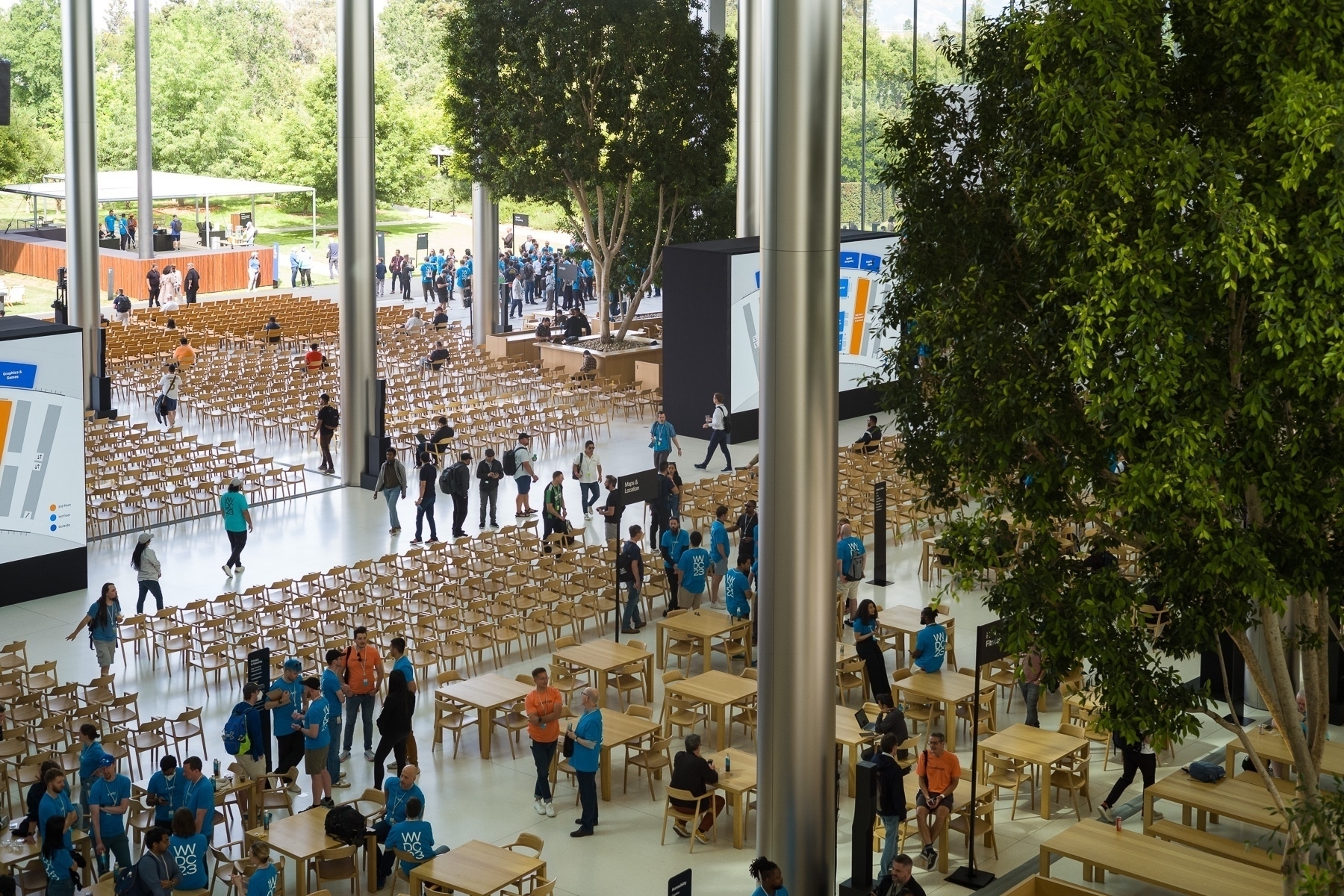 An interior view of a conference area as seen from above. There are a number of chairs, some people, a few style pillars and trees.