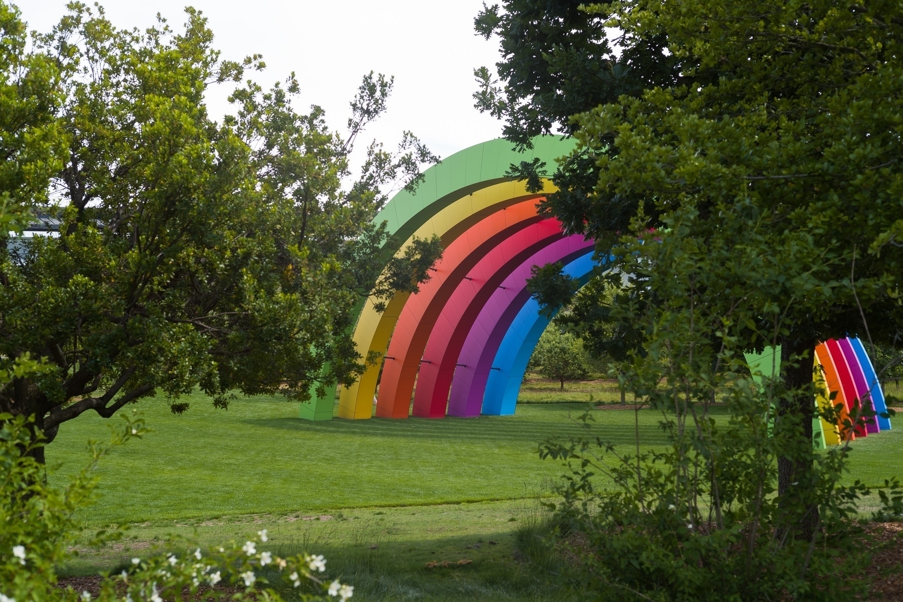 A set of rainbow colored arches are visible in the background with some trees and flowers in the foreground.