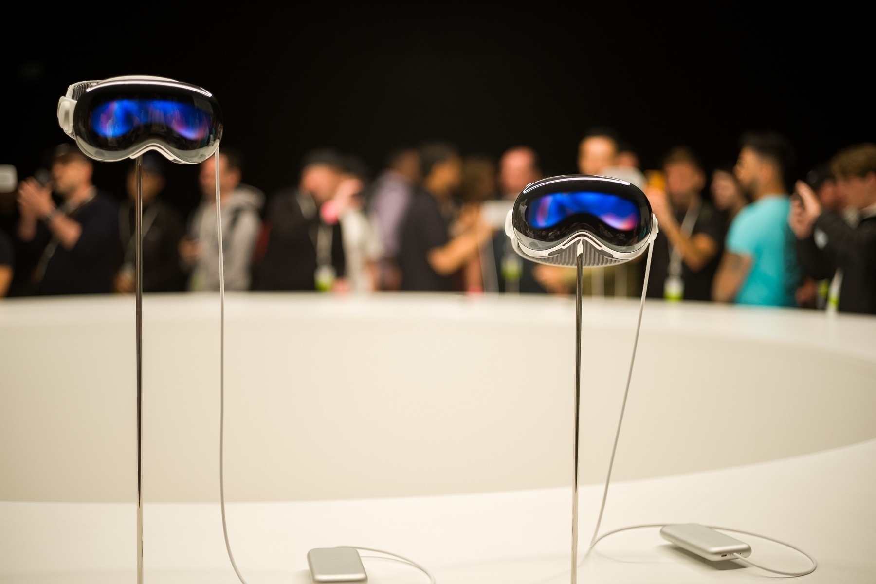 An up-close photo of two Apple Vision Pro devices with people in the blurred background.