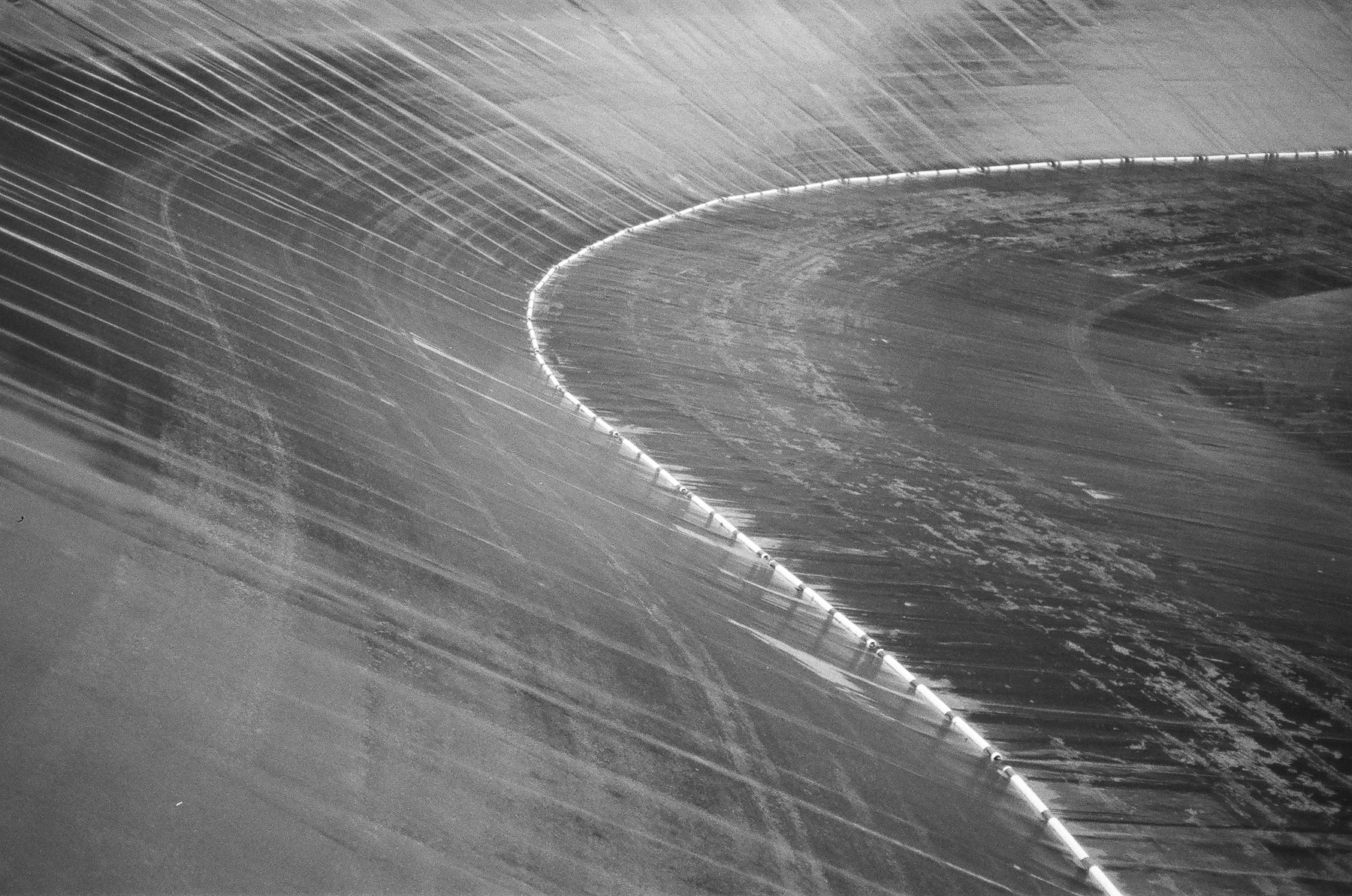 Grainy black and white film photo of an empty reservoir sloping wall with a curved shape.