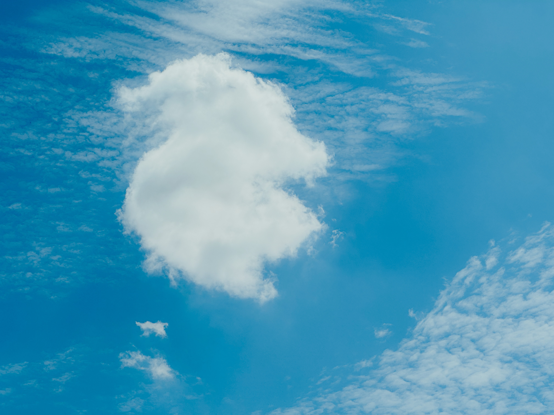 A puffy cloud with blue skies and distant wispy clouds behind it.