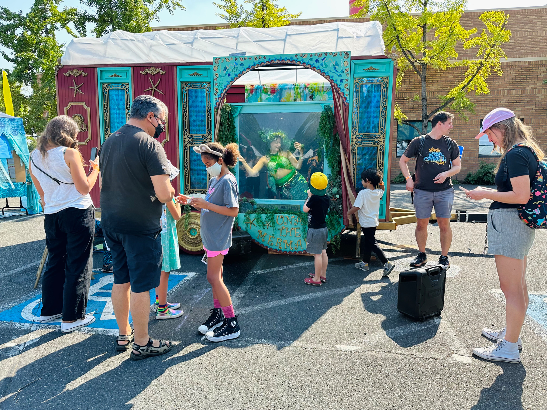 People standing next to a van that has a large window with a water tank and a woman dressed as a mermaid inside it.