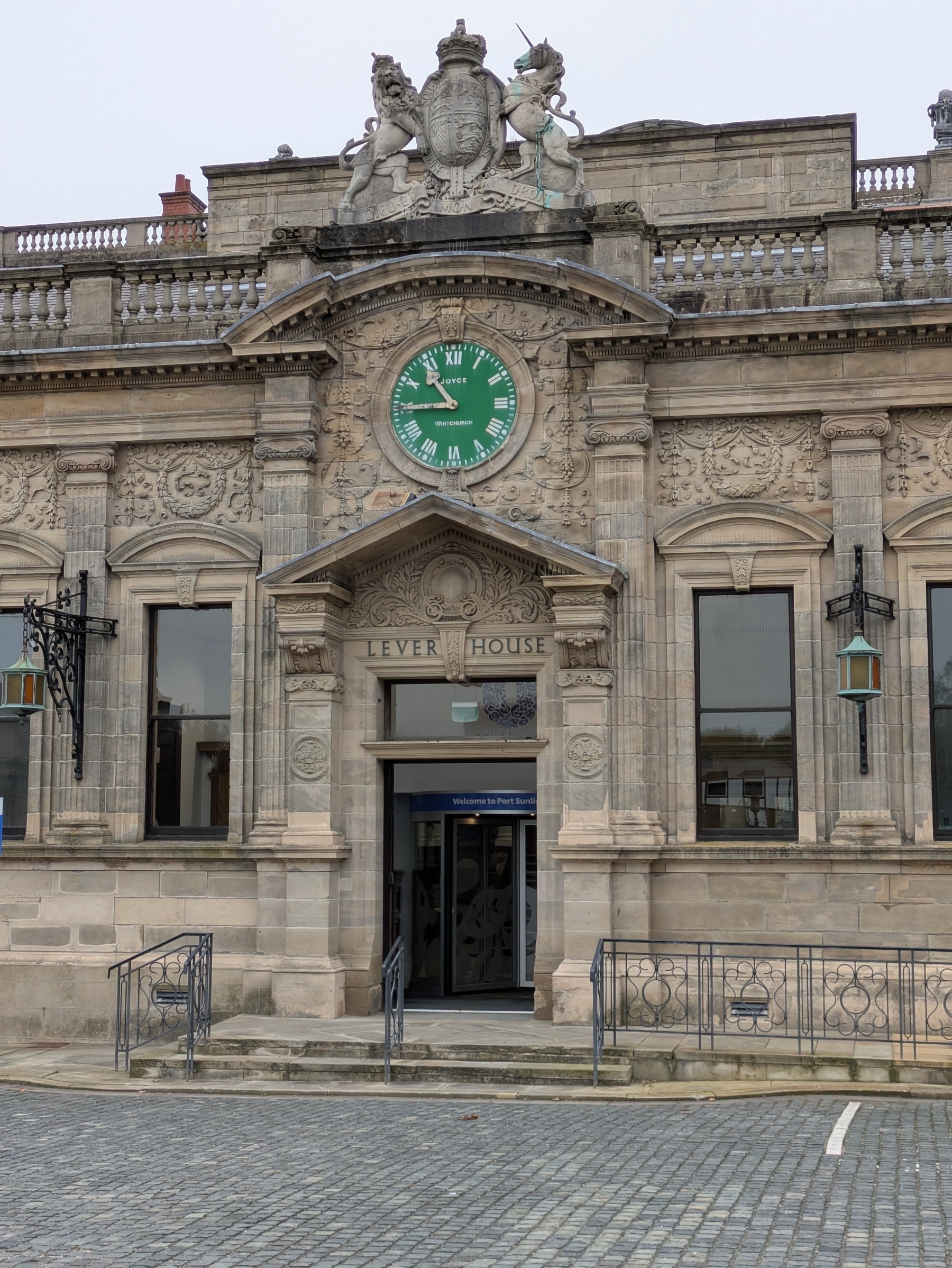 A historic stone building features a prominent green clock and ornately carved details over the entrance labeled Lever House.