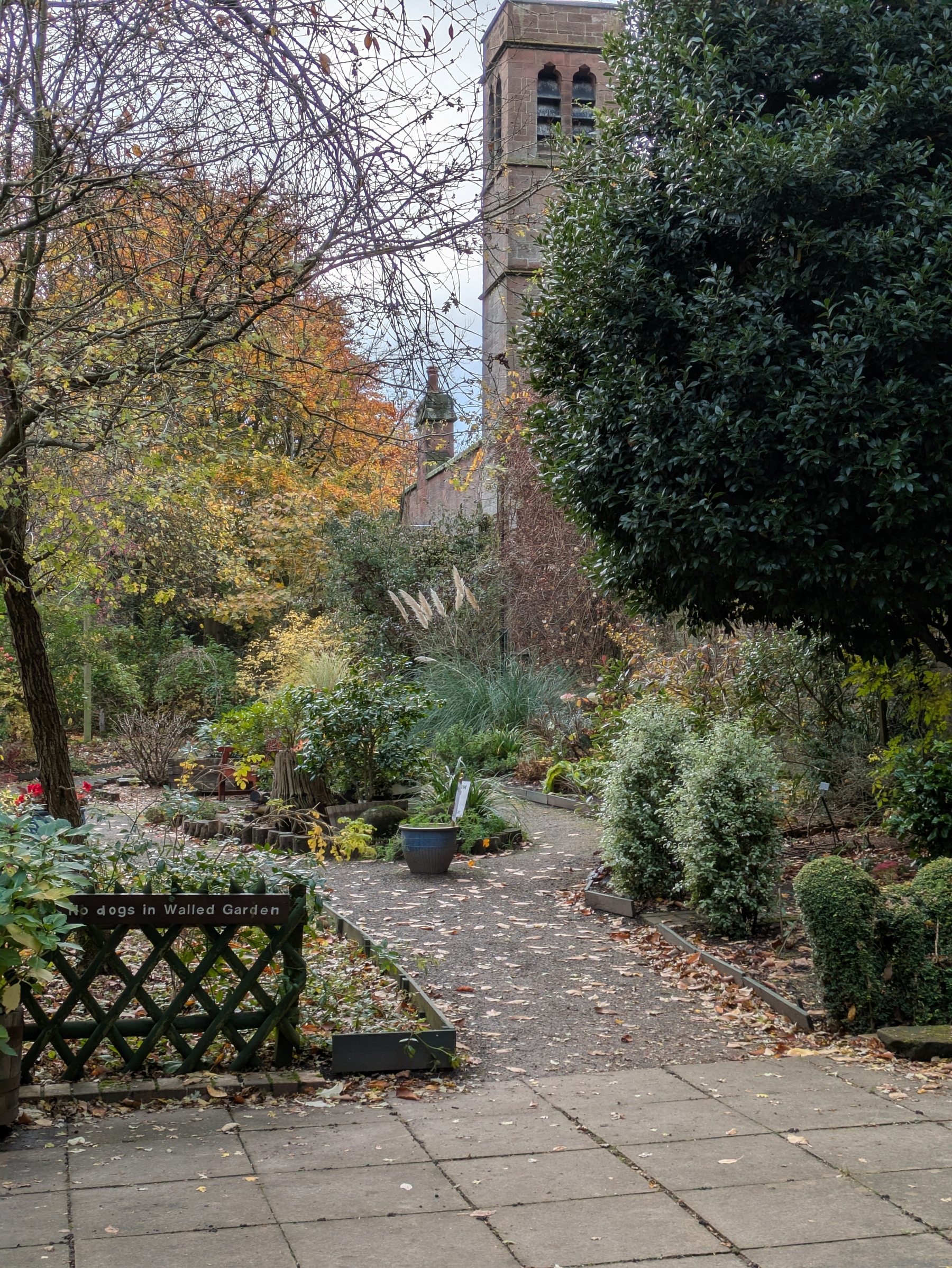 A peaceful garden scene features a pathway surrounded by trees and plants, with an old tower in the background.