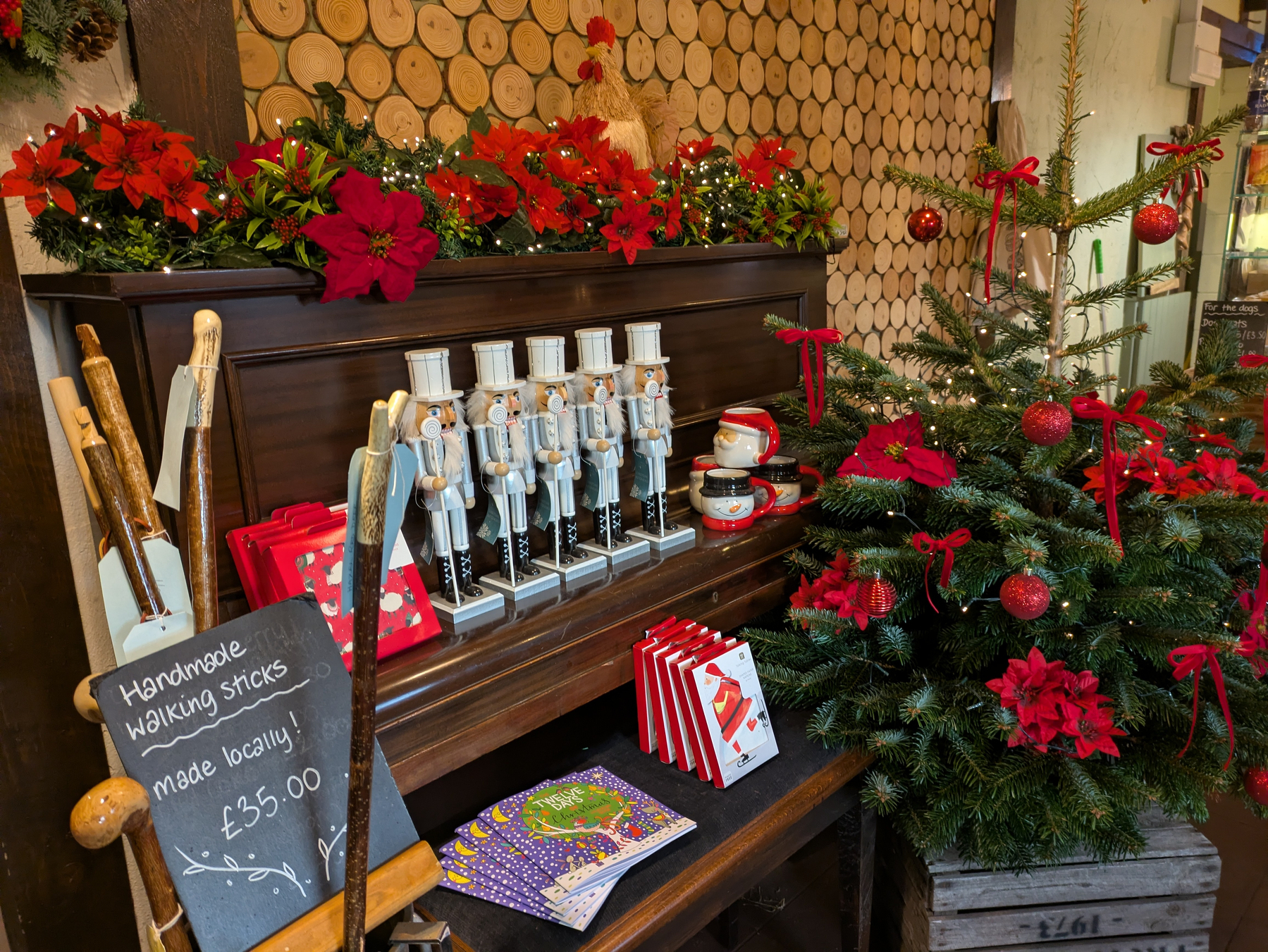 A festive Christmas display features a decorated tree, nutcracker figures, walking sticks, and gifts arranged on an upright piano. 