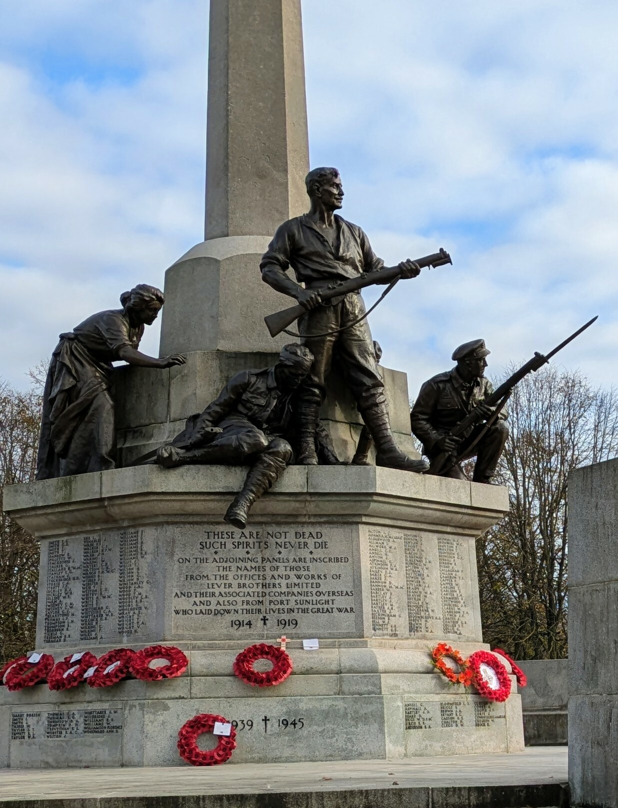 A war memorial featuring statues of soldiers in combat poses adorned with wreaths commemorating both World Wars.