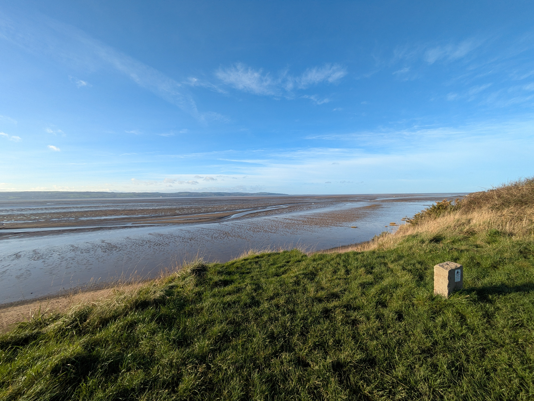 A coastal landscape features grassy cliffs overlooking a wide beach with an expansive sky above.