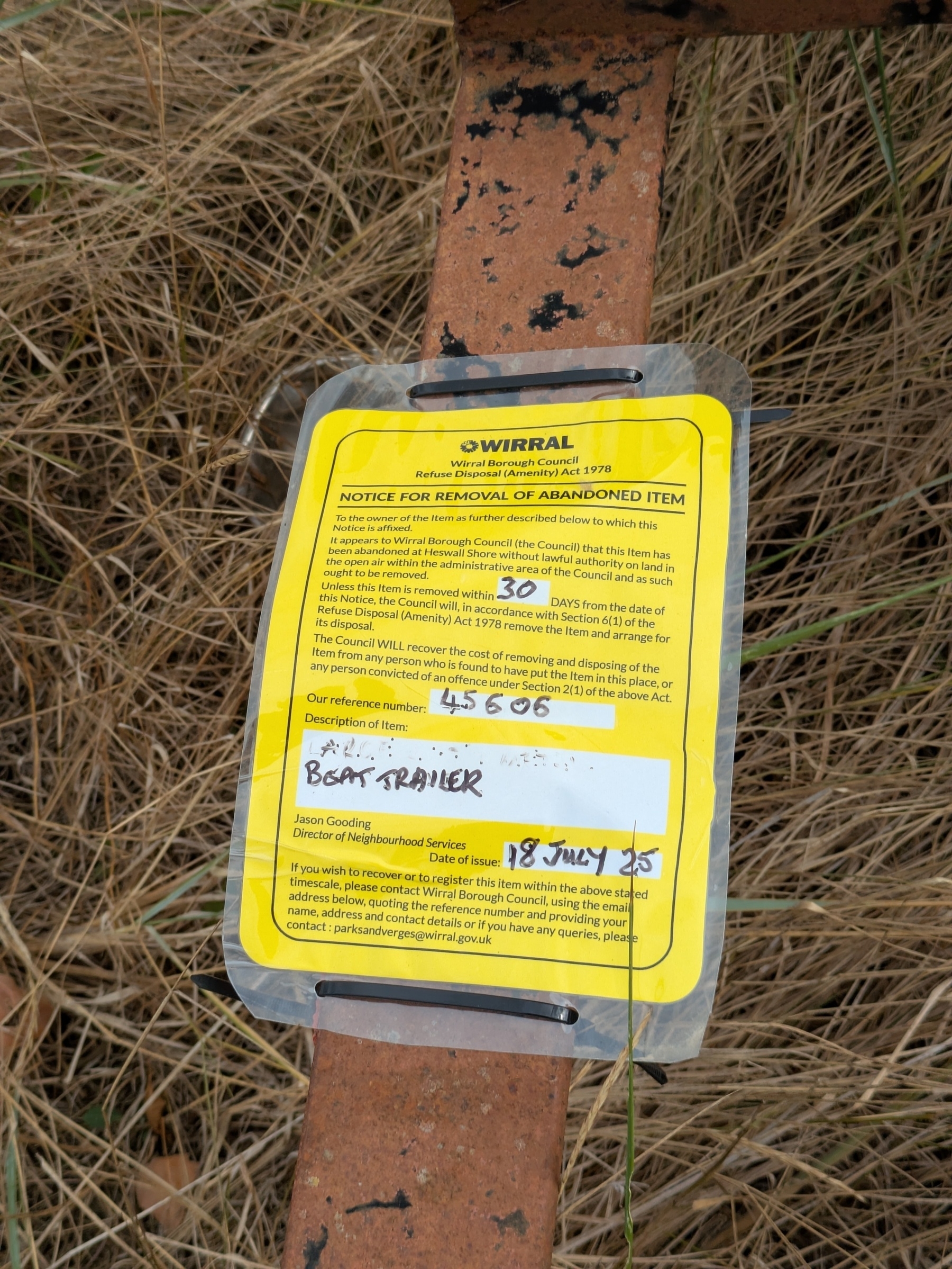 A notice for the removal of an abandoned item, specifically a boat trailer, is attached to a rusty pole.