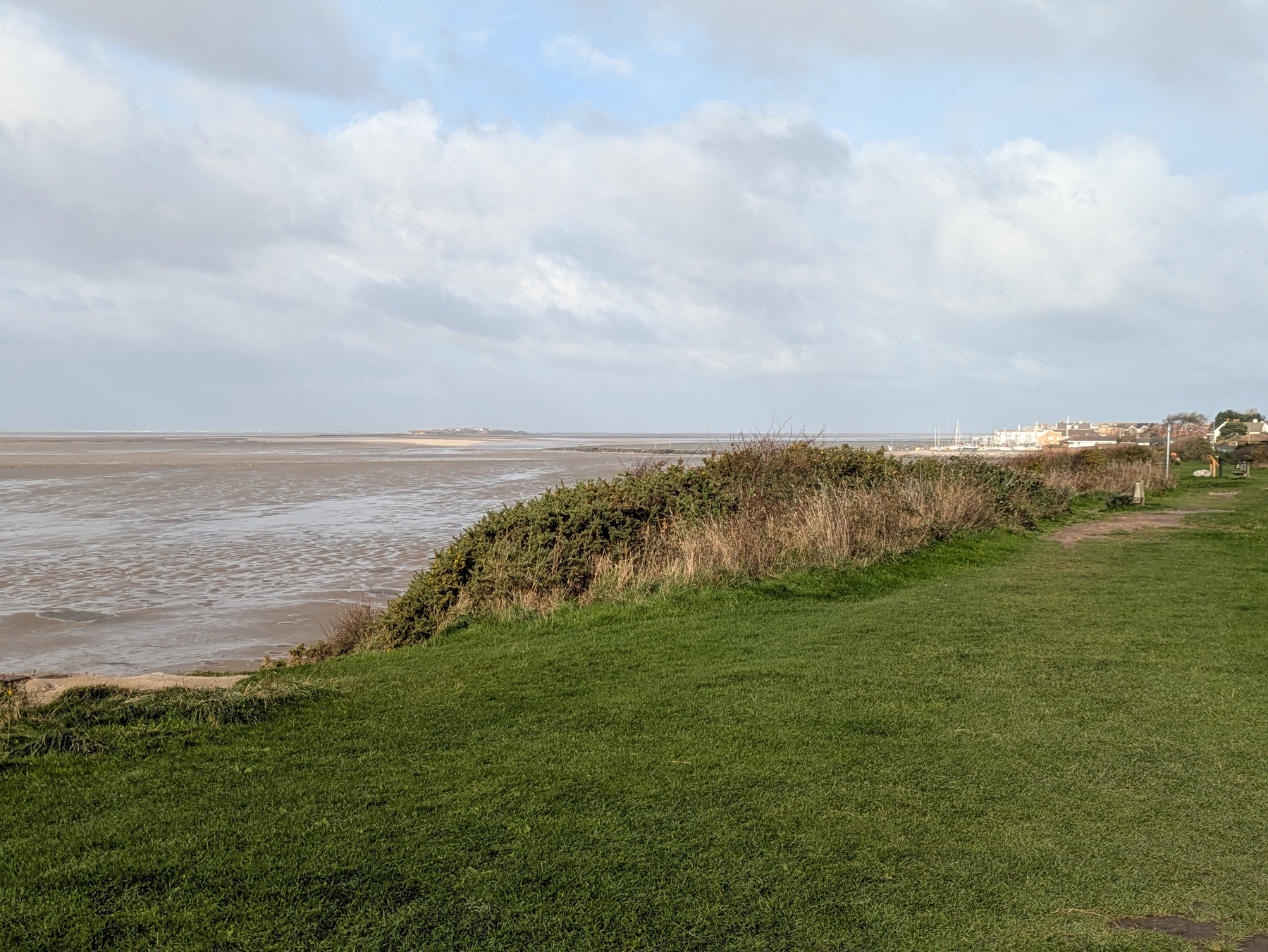 A coastal landscape features grassy fields leading to a sandy beach with cloudy skies overhead.
