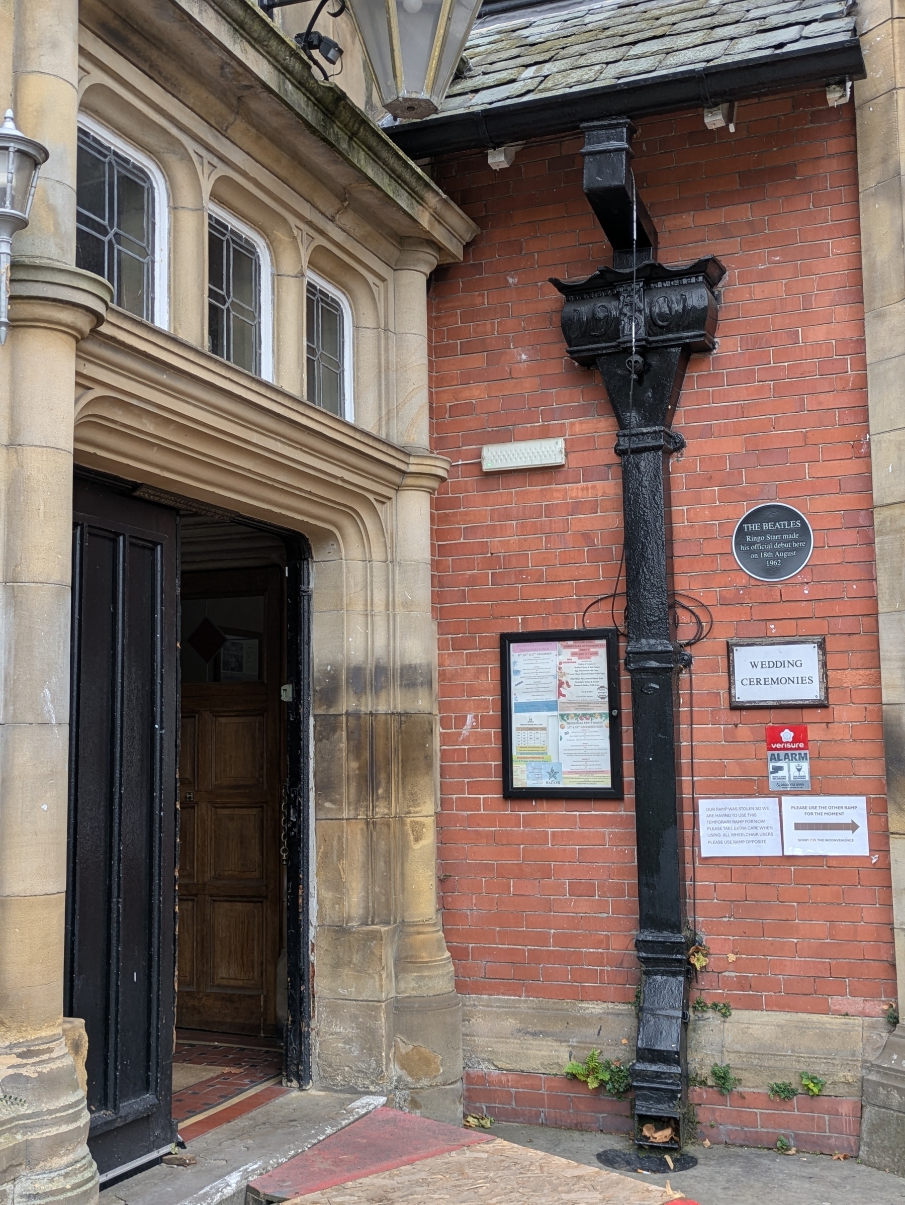 An entrance to a brick building with informational plaques, a drainpipe, and a sign reading Wedding Ceremonies.