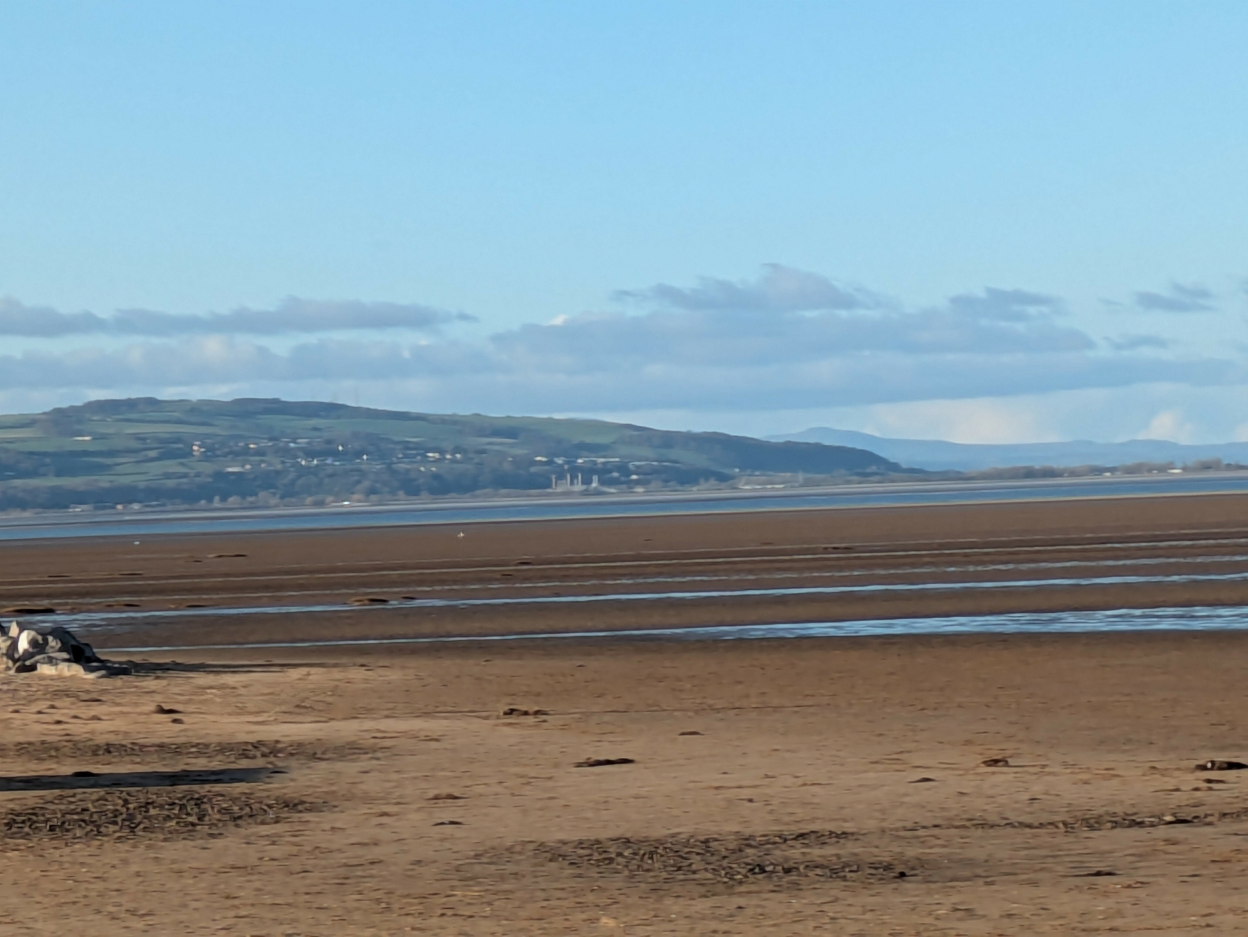 A vast sandy beach stretches toward distant hills under a clear blue sky with scattered clouds.
