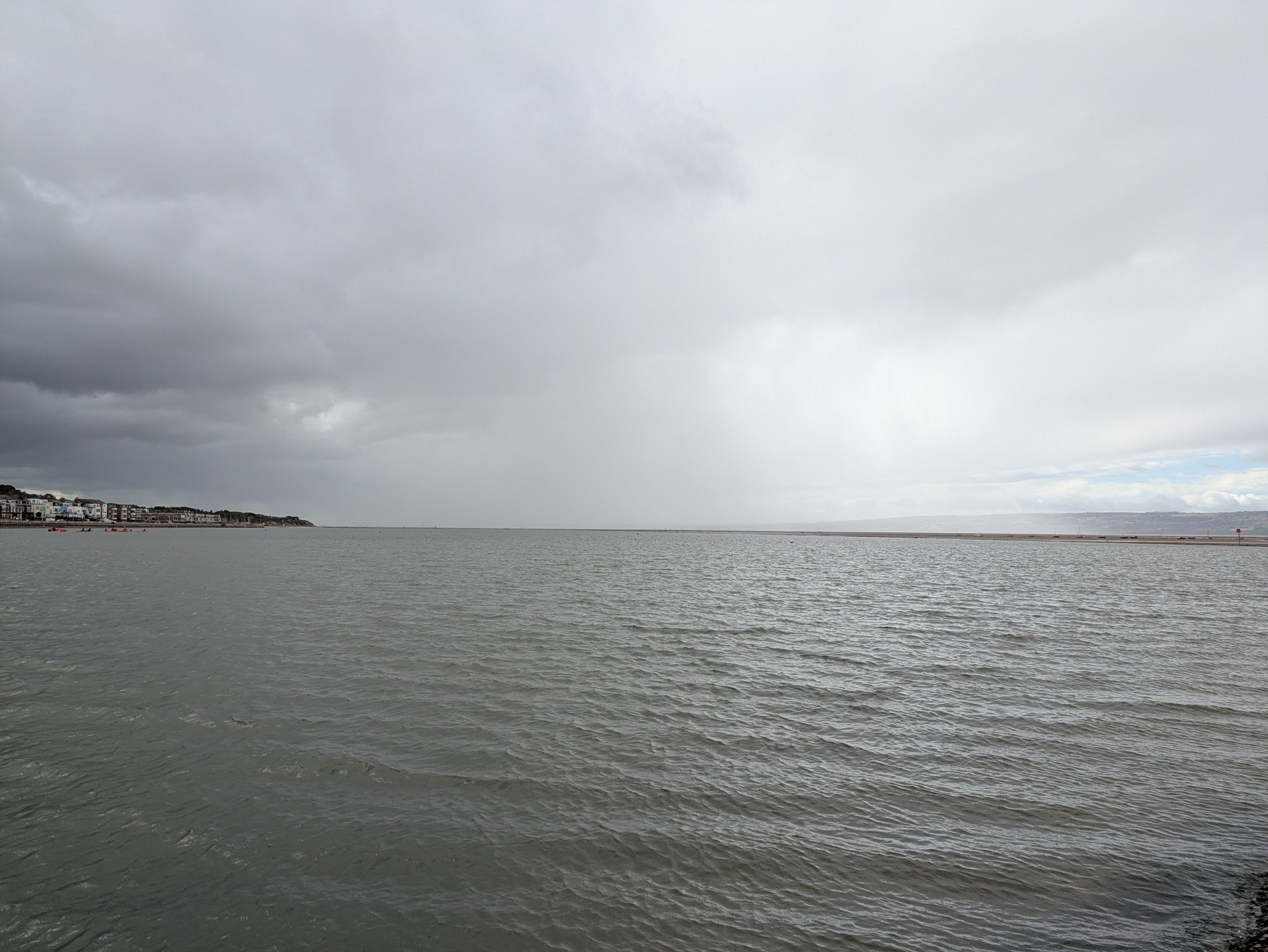 A calm body of water stretches towards the horizon under a cloudy sky, with a distant shoreline visible on the left.