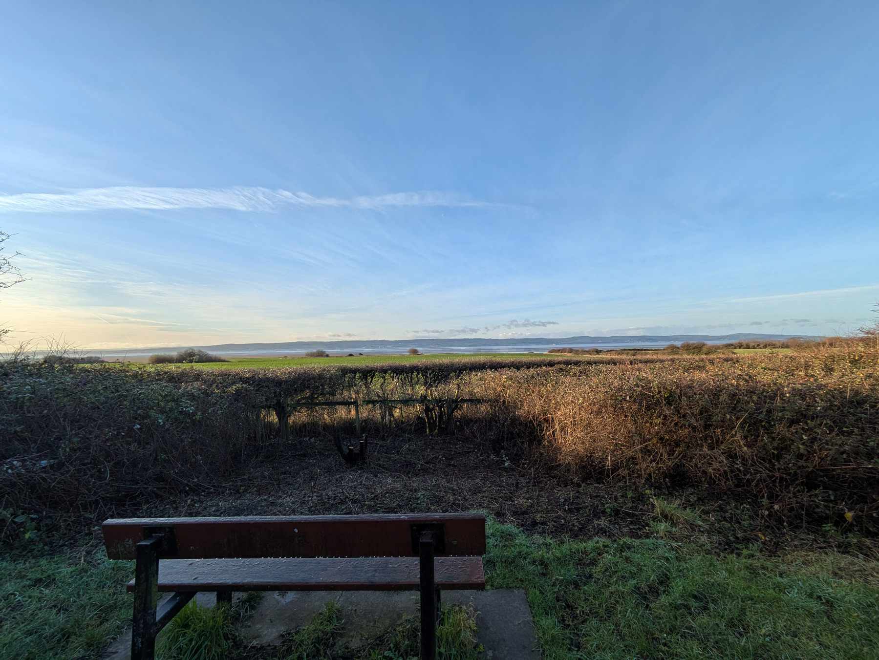 A wooden bench overlooks a vast, open landscape with fields and clear blue skies.
