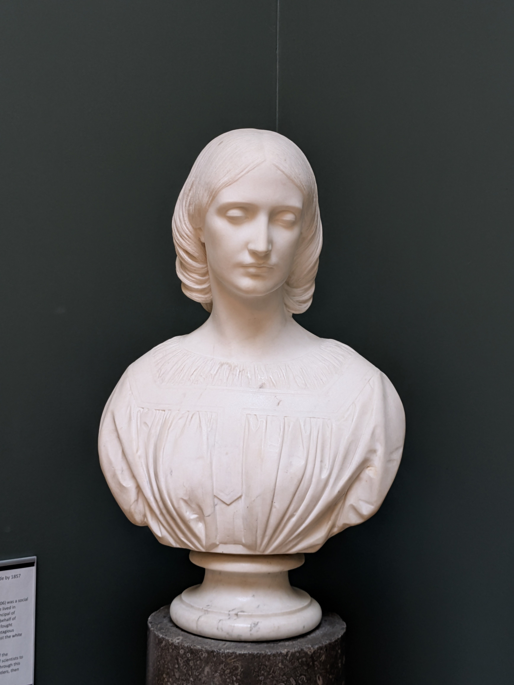 A white marble bust of a Josephine Butler with parted hair and a detailed, pleated dress is displayed against a dark background.