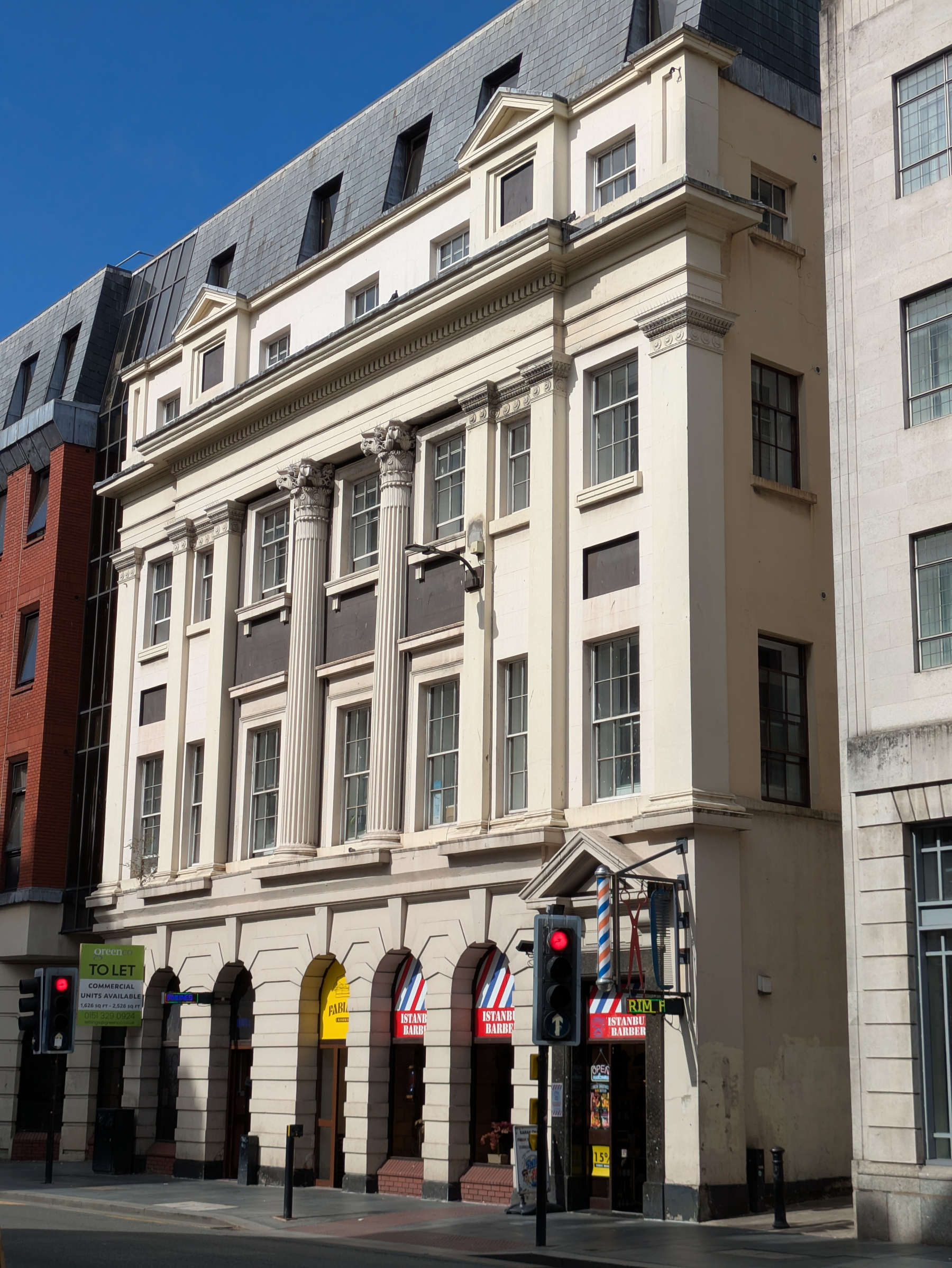 A multi-story historic building with classical columns houses a barber shop at street level and is situated on a city street corner with traffic lights.