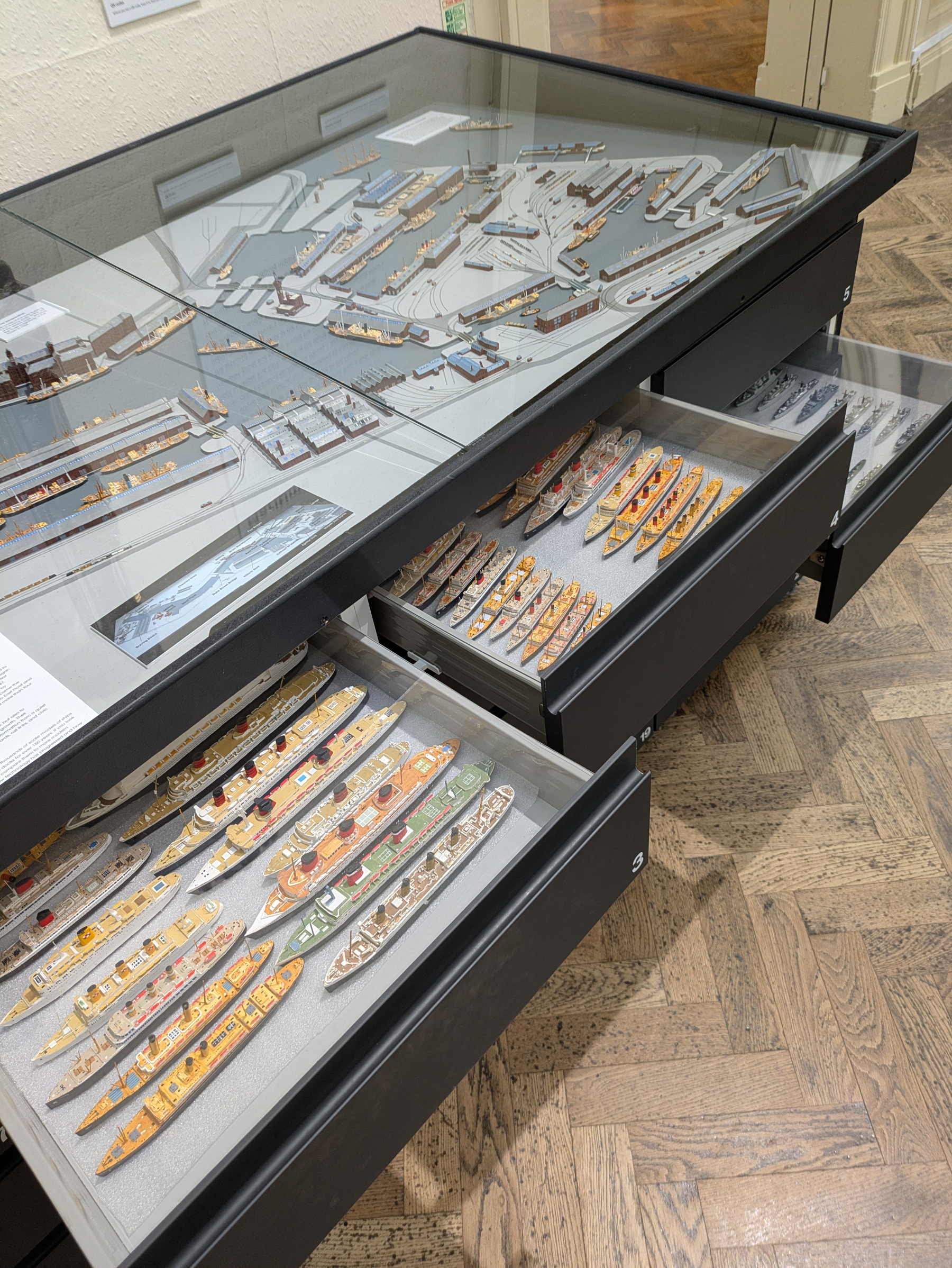 A display case and drawers contain detailed miniature ship models and a layout of a dockyard or harbor.