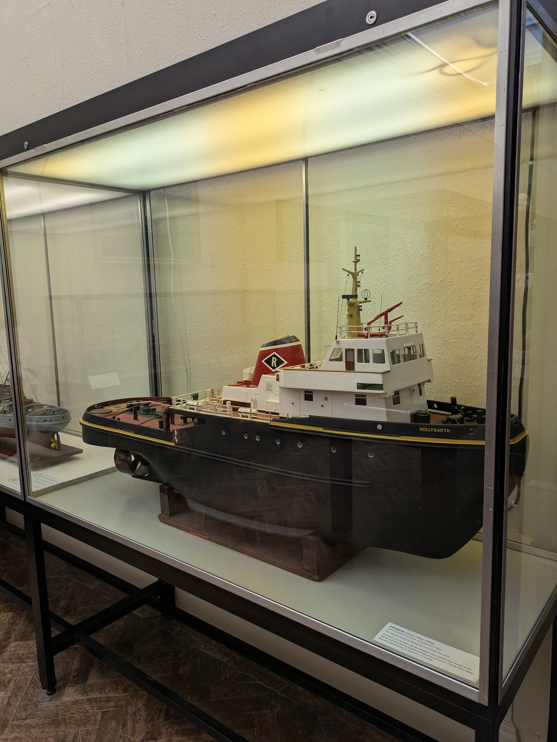 A detailed scale model of a tugboat named Hollygarth is displayed inside a glass case.