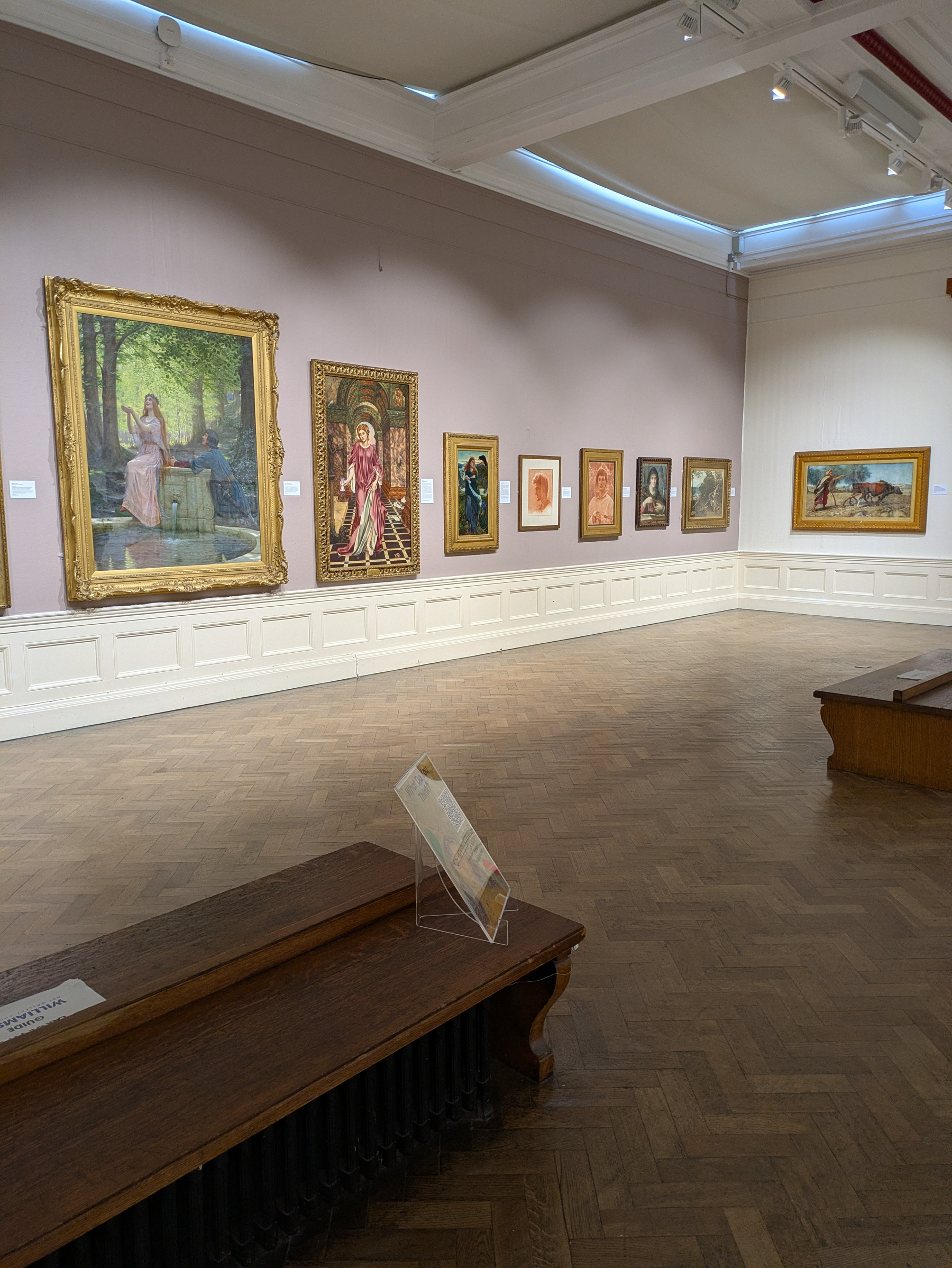 A quiet art gallery room features a series of framed paintings displayed with benches for visitors to sit and appreciate the artwork.