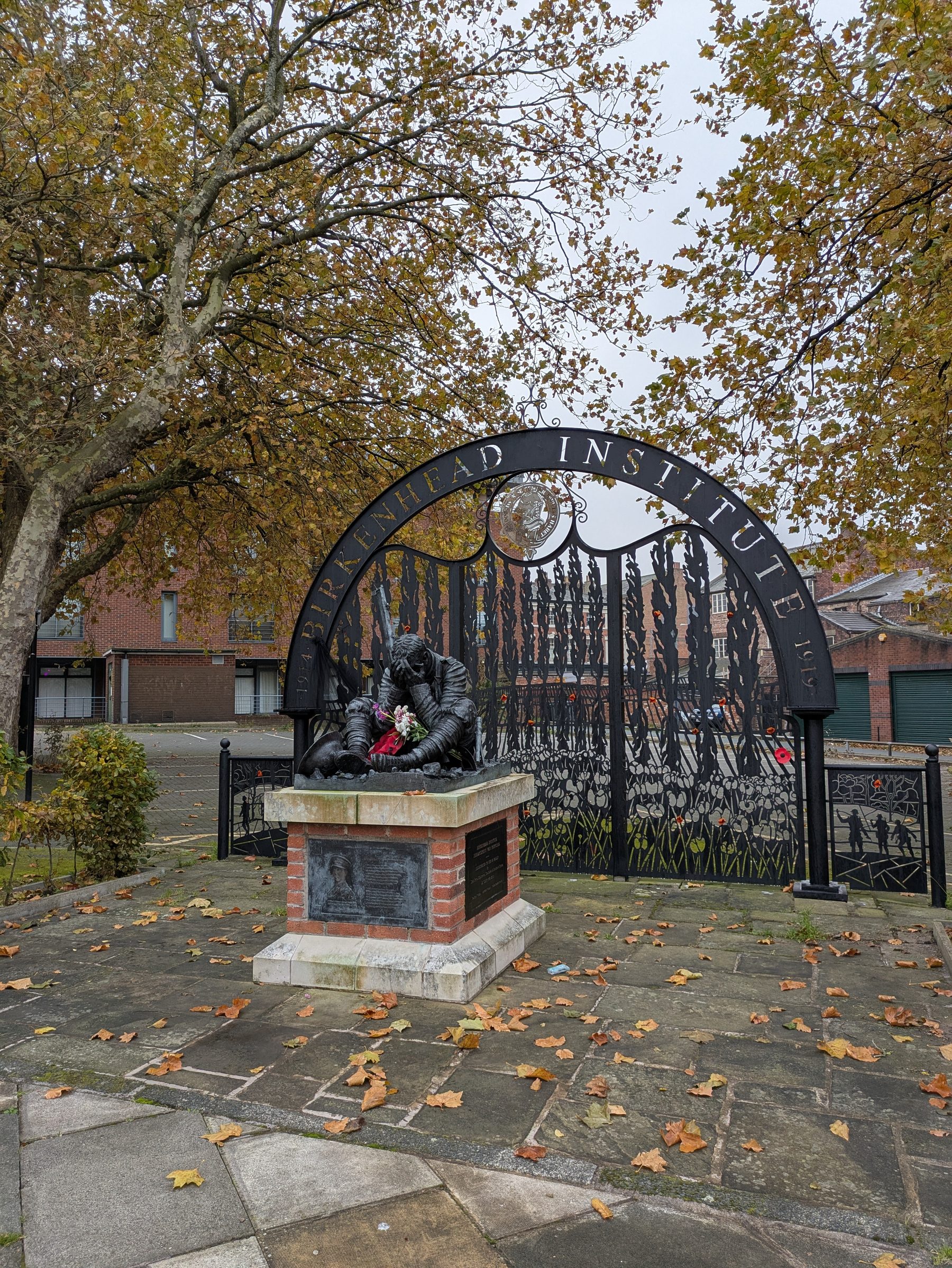 A statue of a seated soldier with a real bouquet of flowers rests in front of a decorative archway labeled Birkenhead Institute.