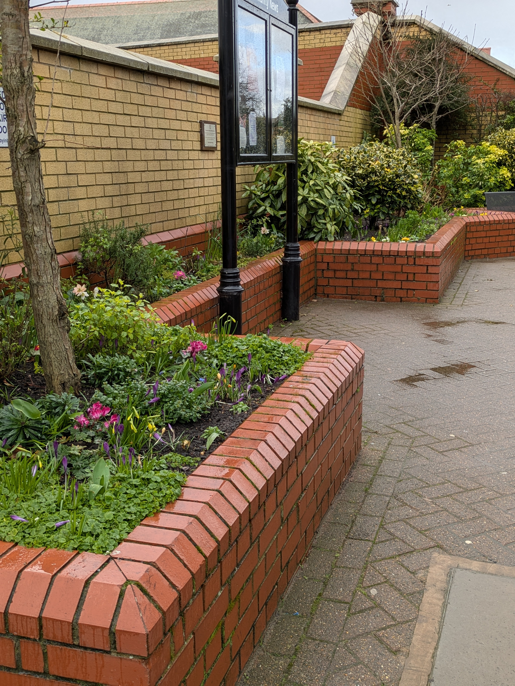 A landscaped area features brick planters filled with various plants and flowers along a paved pathway.