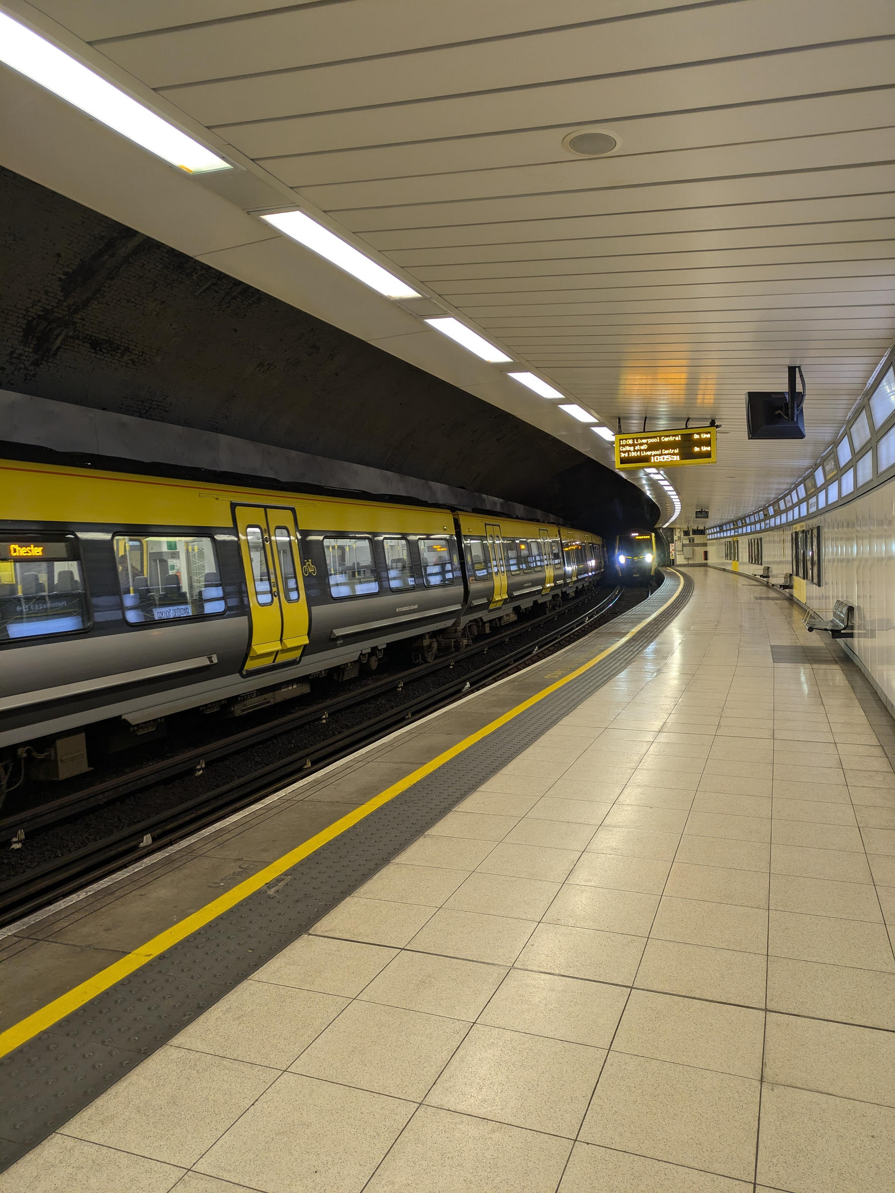 A train is arriving at an empty, modern underground station with a curved platform and overhead lighting.