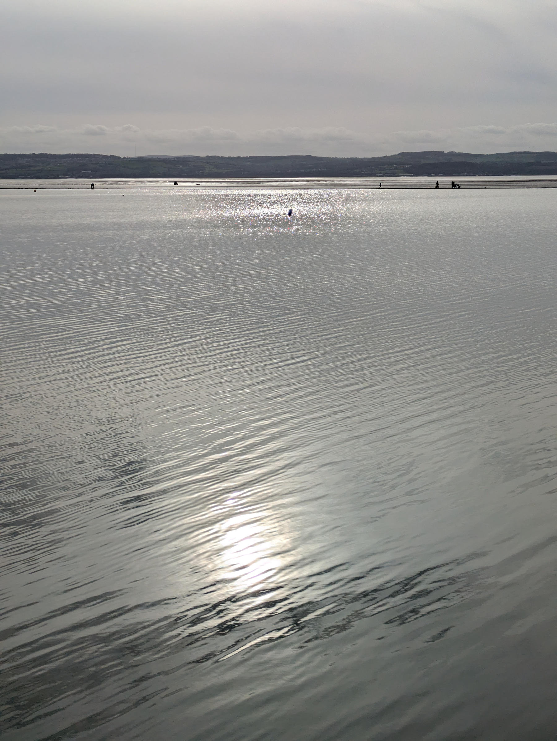 A serene body of water reflects the sunlight under a cloudy sky with distant hills on the horizon.