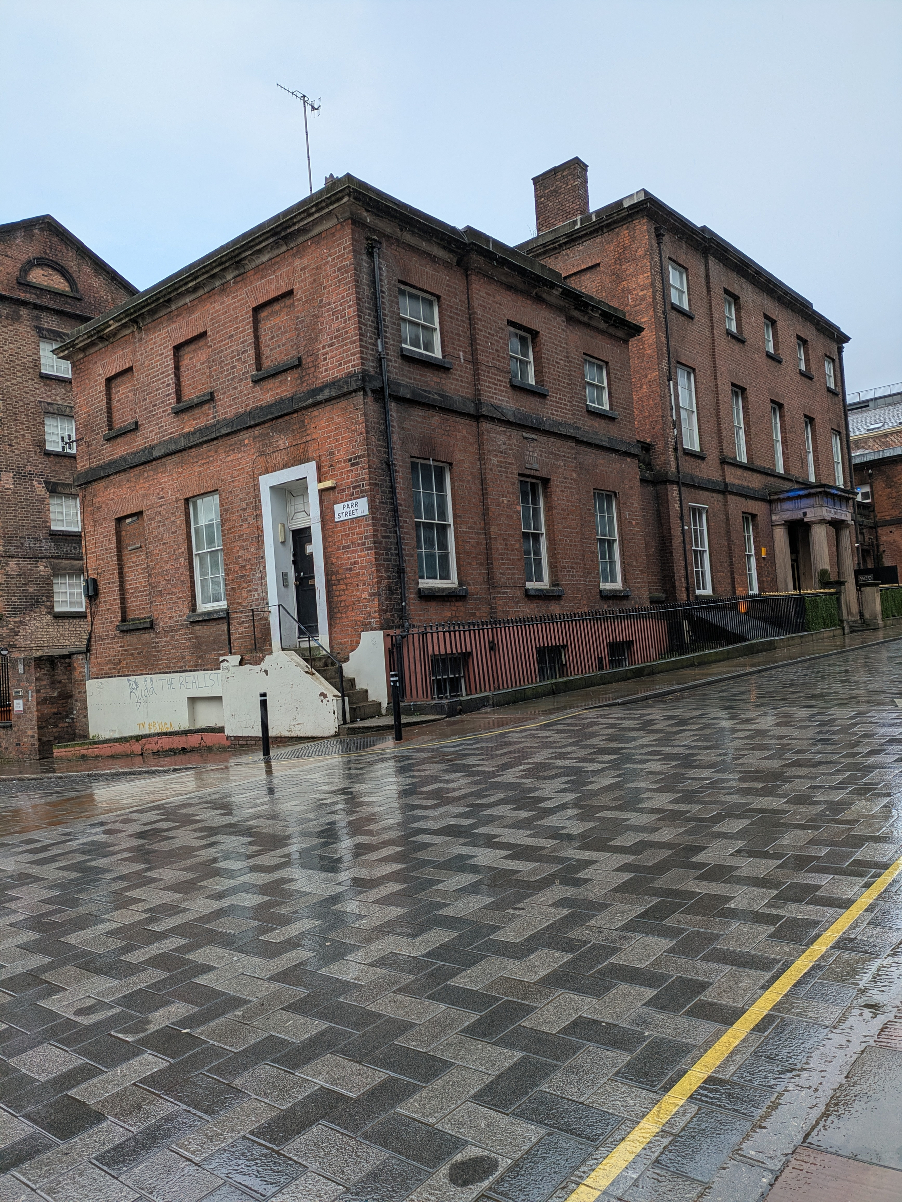 A brick building on a rainy day stands beside a wet cobblestone street.