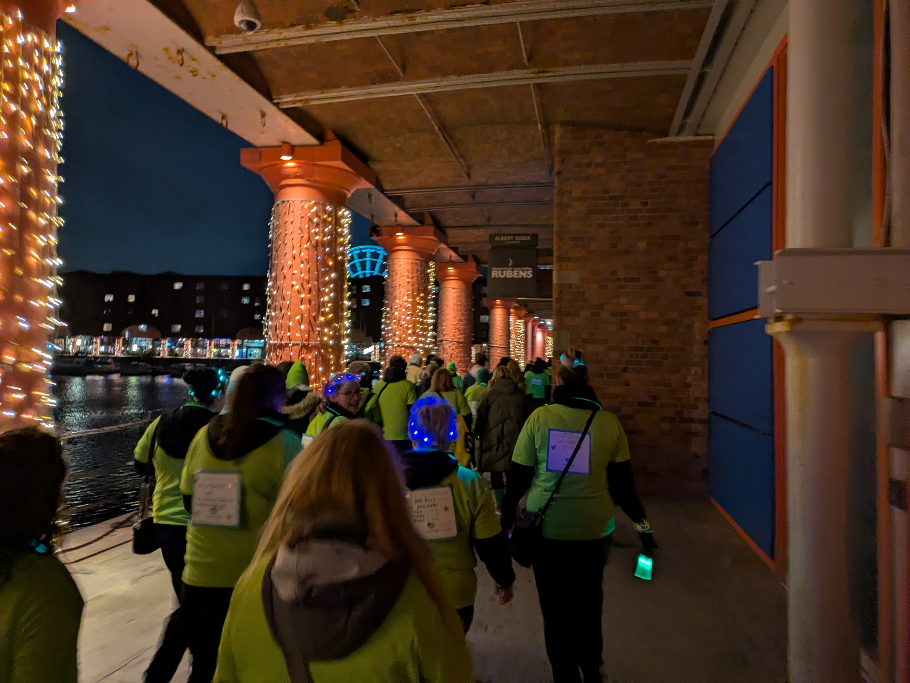 People wearing green shirts walk along a decorated pathway with string lights at night.
