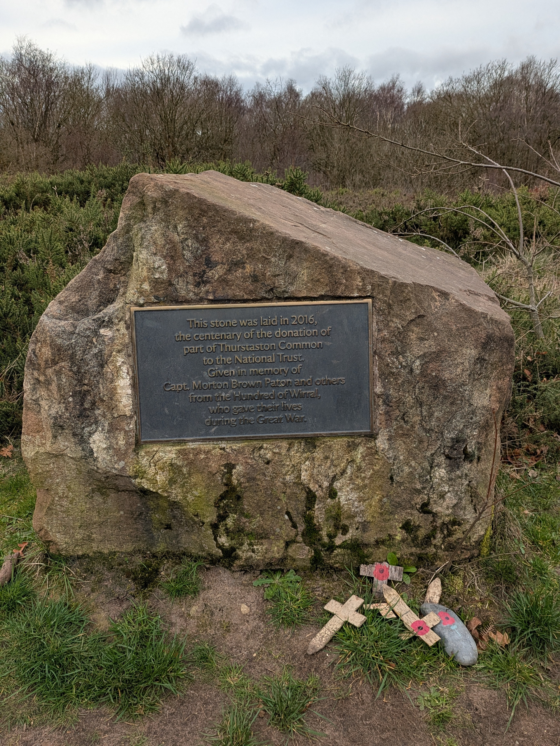 Auto-generated description: A commemorative stone from 2016, honoring the donation of Thurstaston Common to the National Trust, is adorned with a plaque and small memorial crosses.