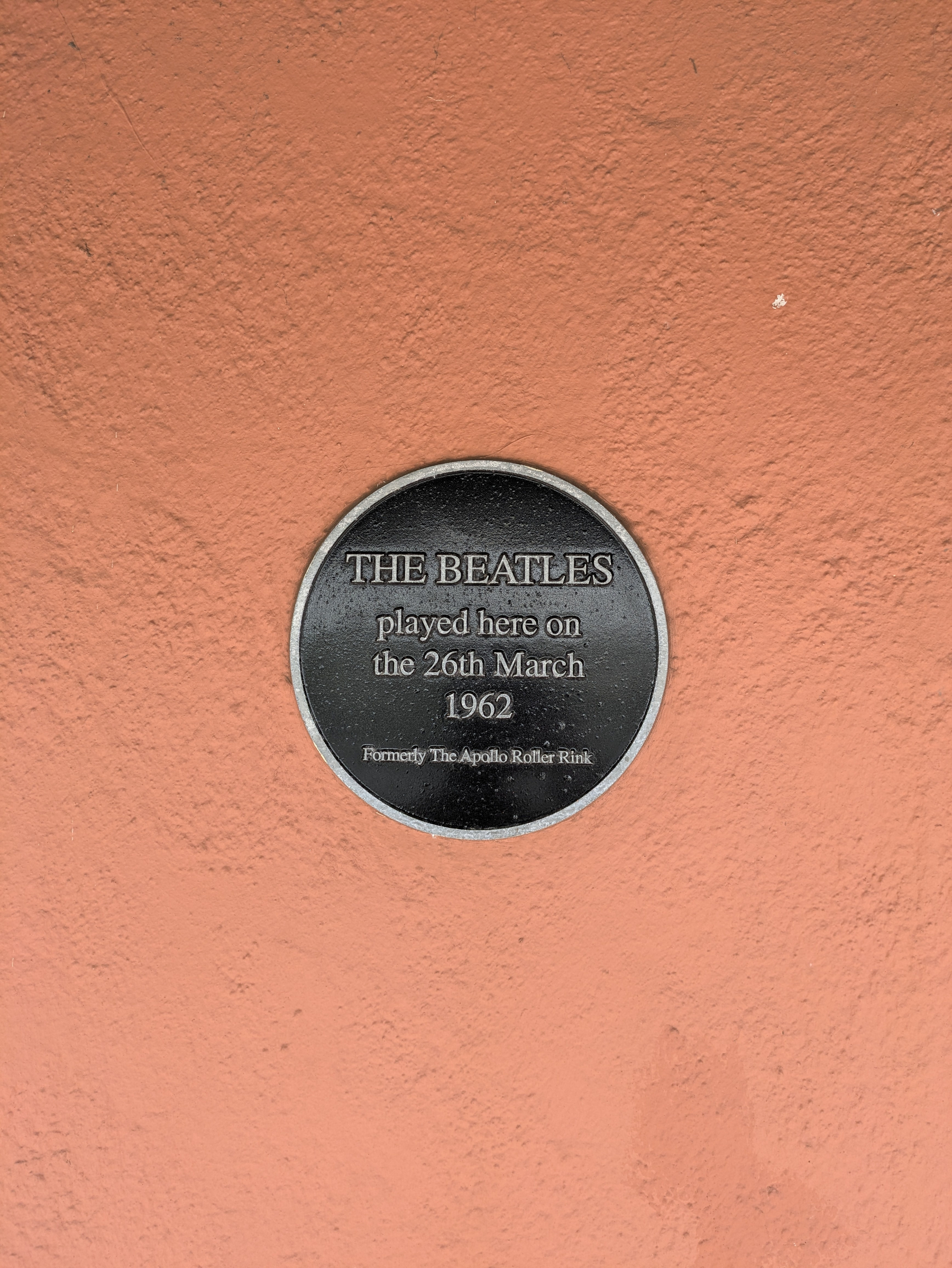 A circular plaque on a brick wall commemorates The Beatles' performance on March 26, 1962, at the former Apollo Roller Rink.