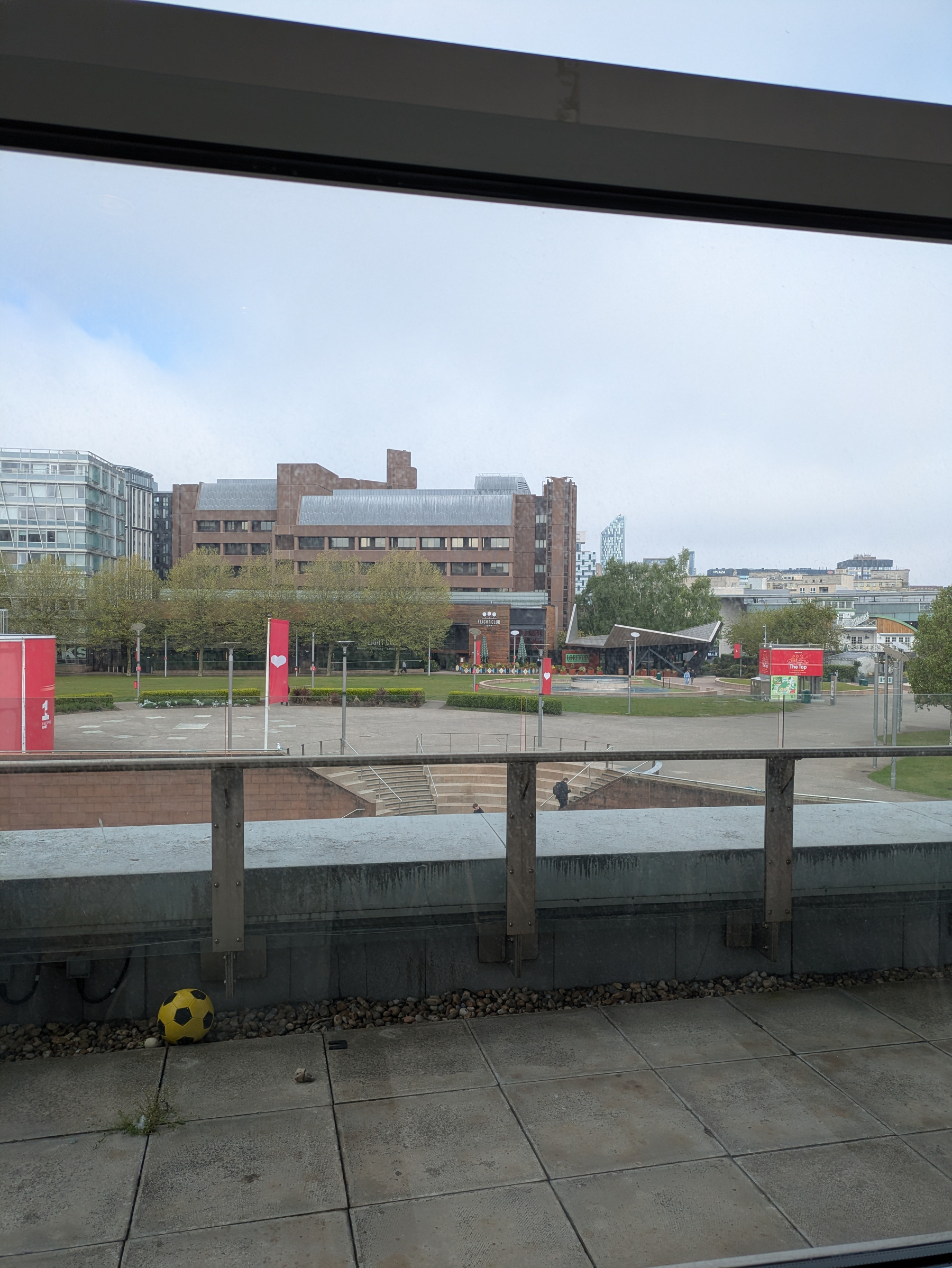 A cityscape view shows a brick building, surrounding trees, red banners, and an empty courtyard with a lone soccer ball on a concrete patio.