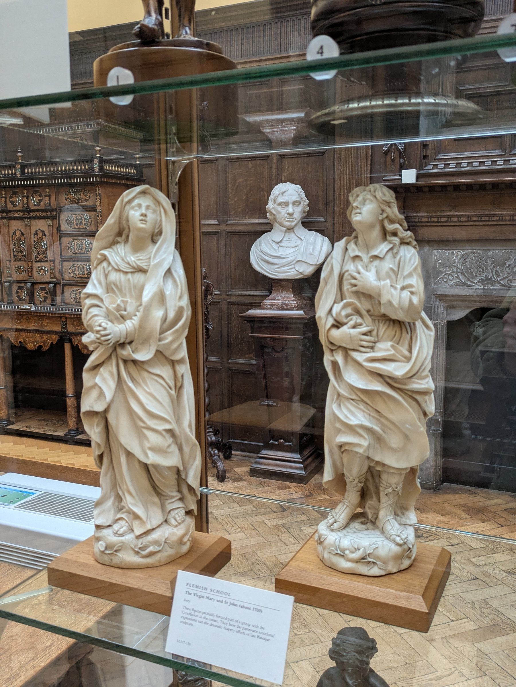Two intricately carved statues are displayed in a glass case, set against an ornate wooden interior.
