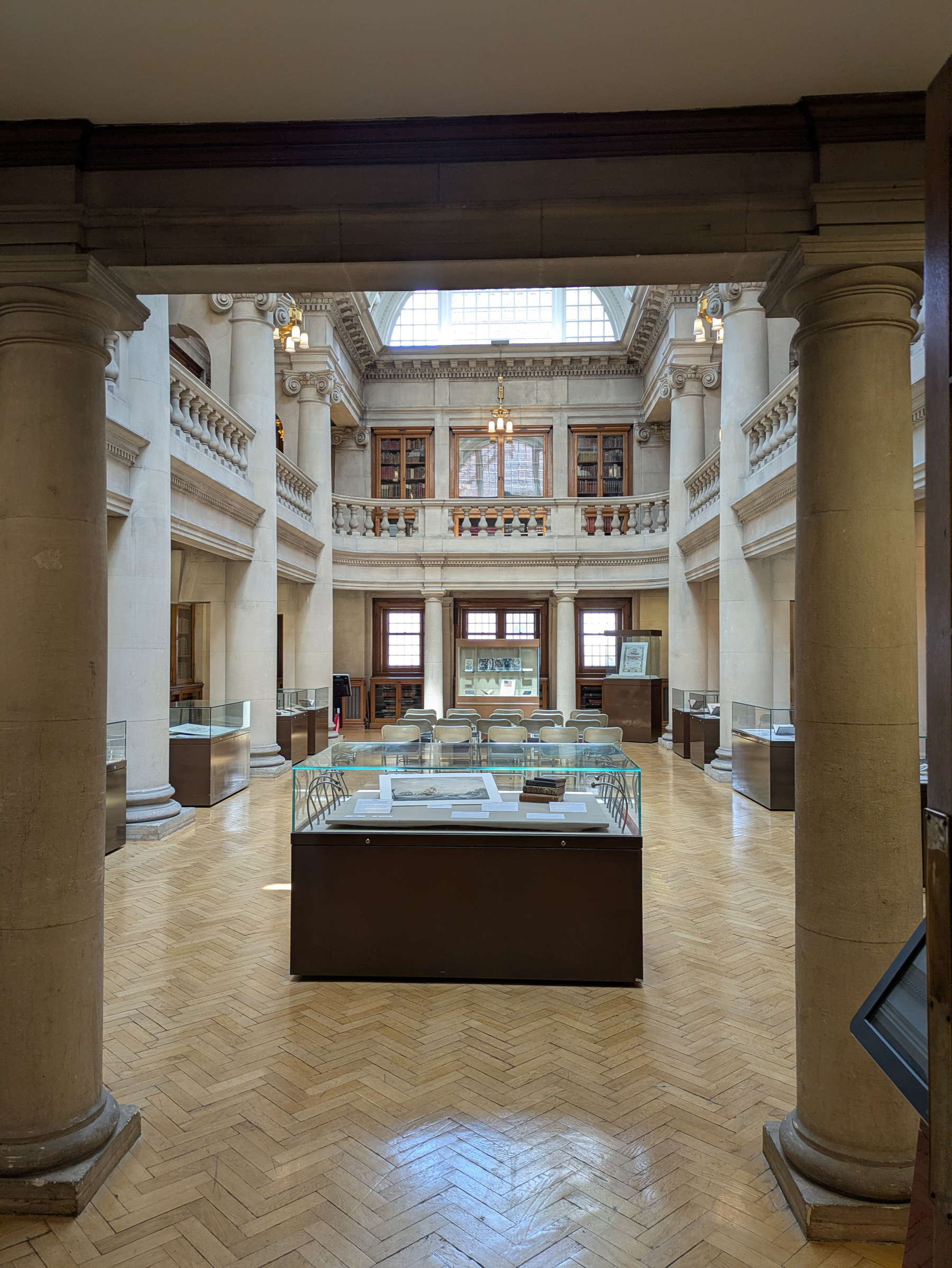 A grand, well-lit room with classical architecture features display cases and ornate columns.