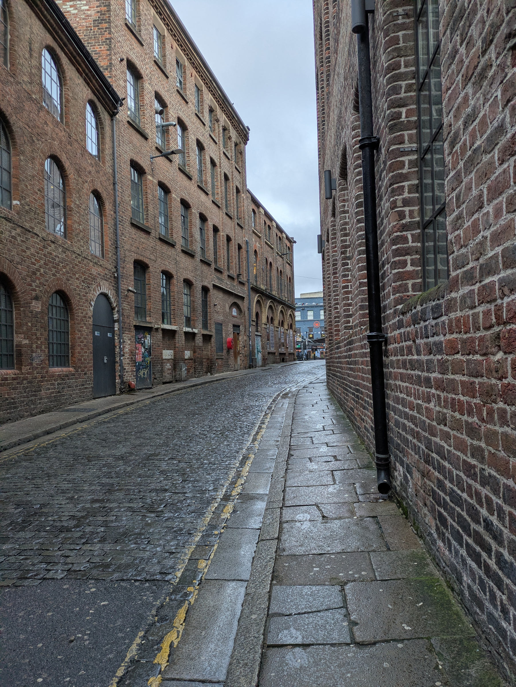 A narrow cobblestone street is lined with tall, old brick buildings under a cloudy sky.