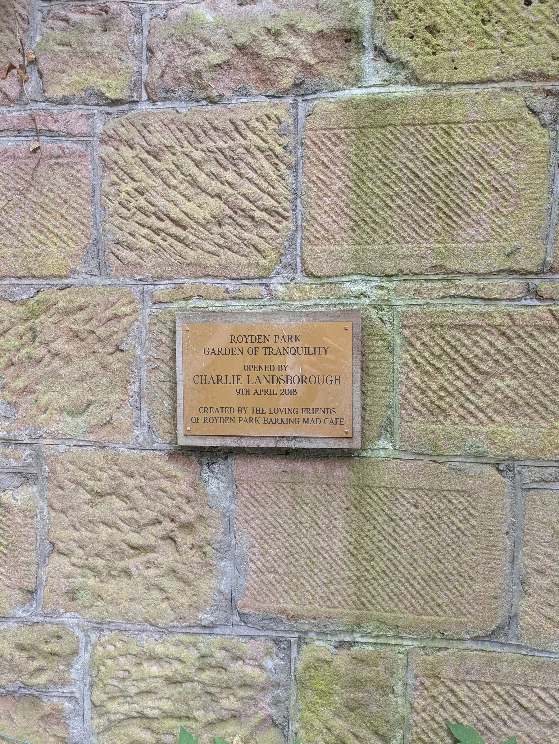 A plaque on a stone wall commemorates the opening of Royden Park Garden of Tranquility by Charlie Landsborough on 9th April 2018, created by the loving friends of Royden Park Barking Mad Cafe.