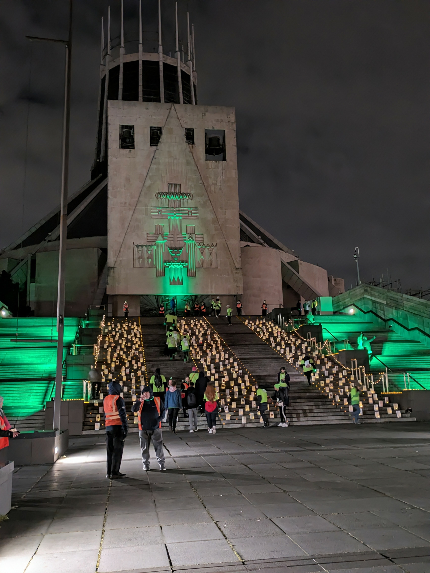 People are setting up illuminated displays on the steps of a church with green lighting at night.